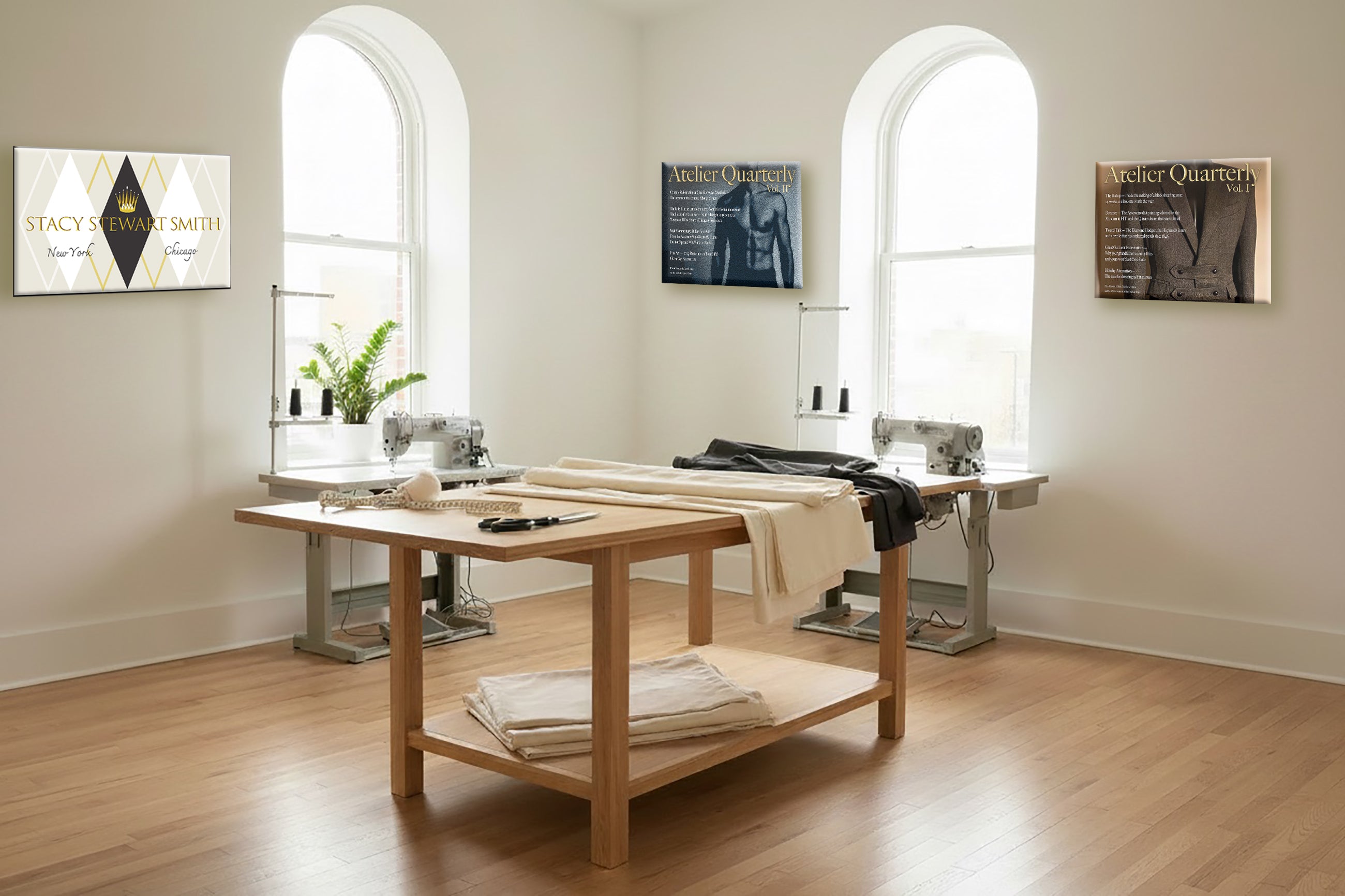 Stacy Stewart Smith's  bright, modern sewing studio with light wood floors, featuring a central wooden work table with fabric and a sewing machine on top, flanked by two arched windows and framed wall art.