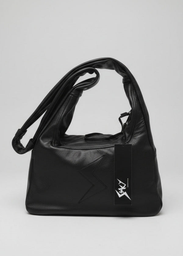 Stacy Stewart Smith Trapezoid Leather Messenger Bag in Onyx with the strap folded over the left top in front of a light gray backdrop.
