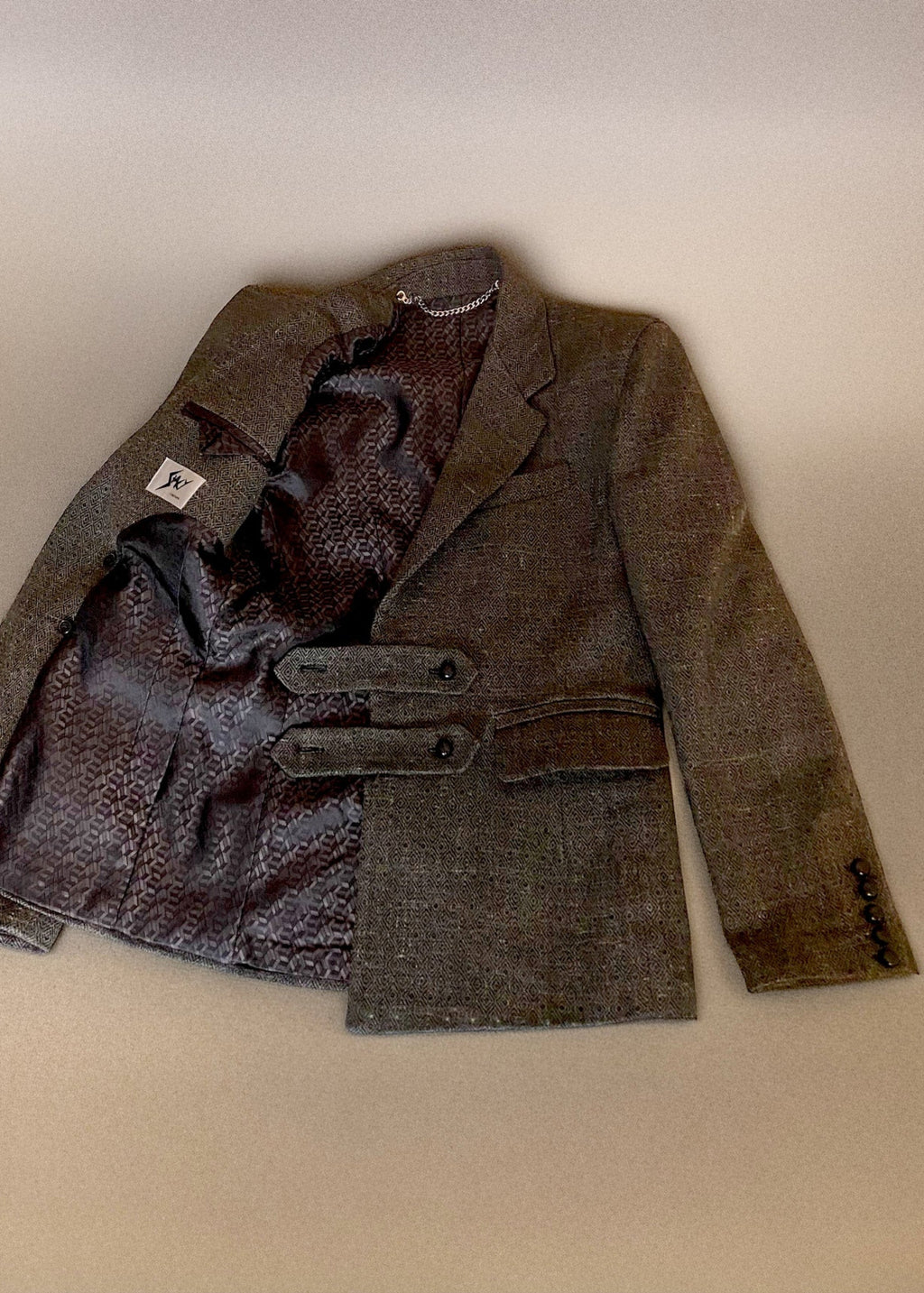 Stacy Stewart Smith Men's Highland Gentry Diamond Tweed Suit lying flat with one side of the front open revealing the box pattered acetate lining, the Stacy Couture brand label and chain hanging accessory on an Ivory shadowed paper surface. 