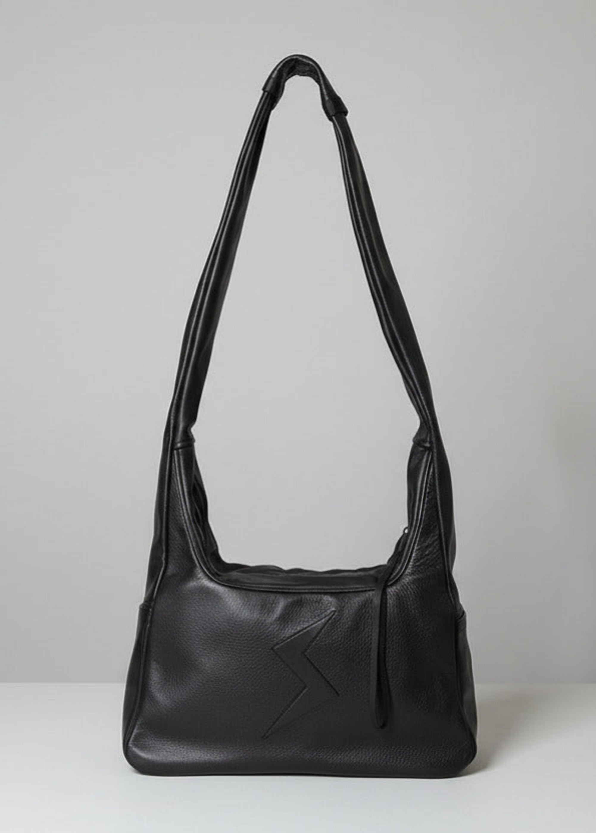 Stacy Stewart Smith Trapezoid Leather Messenger Bag in Onyx front view with the strap standing up in front of a light gray backdrop.
