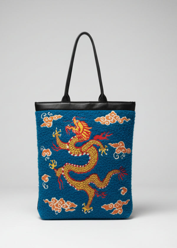 Front view of Stacy Stewart Smith's Lagoon Blue Chenille Dragon & Ruby Tote shows Frolicking, Oriental dragon embroidery, mango cloud embroidery, black leather handle and lips against a white backdrop. 