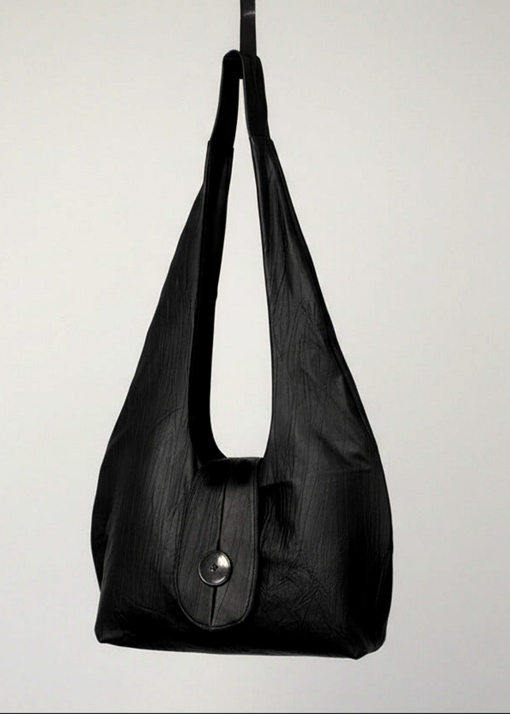 Stacy Stewart Smith Euclidian Space Crinkled Leather Messenger Bag frontal view hanging from a hook in front of a white backdrop.