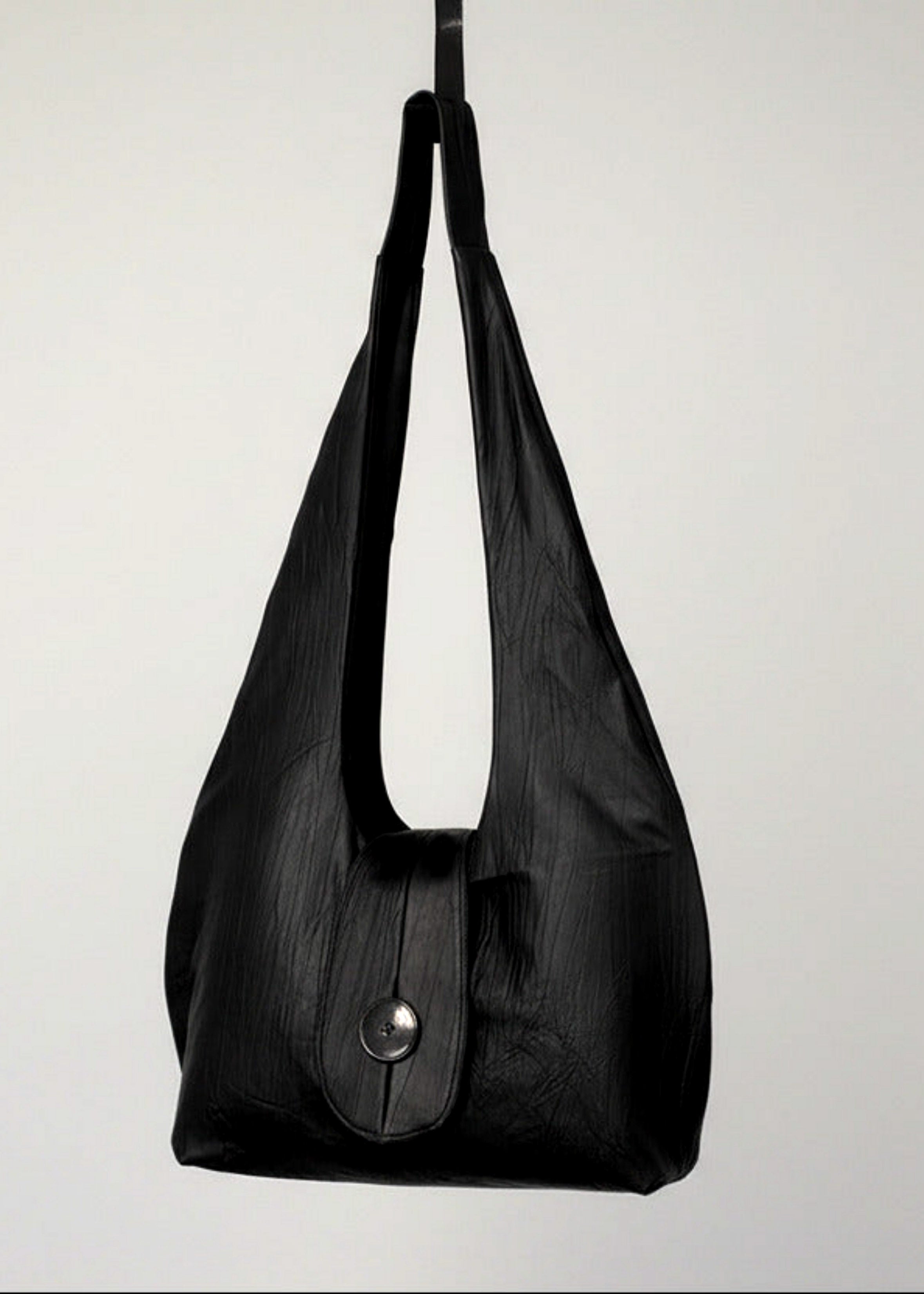 Stacy Stewart Smith Euclidian Space Crinkled Leather Messenger Bag frontal view hanging from a hook in front of a white backdrop.