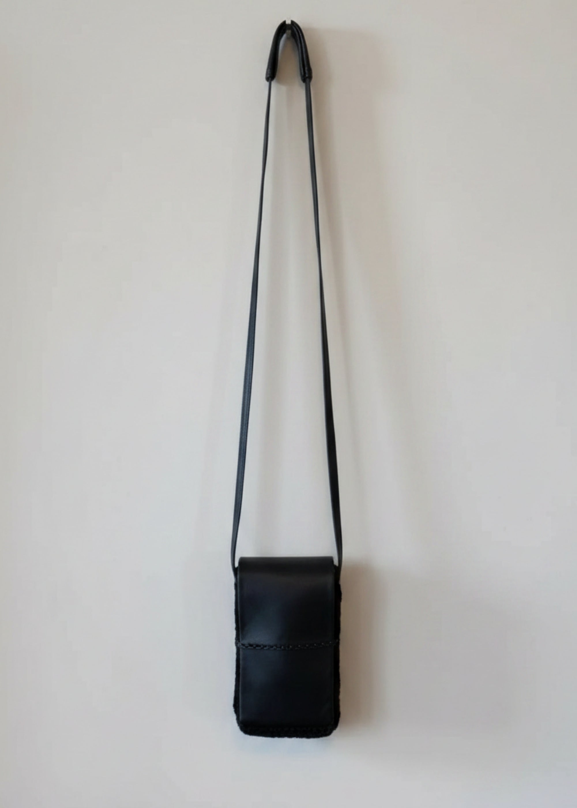 Stacy Stewart Smith Onyx Persian lamb and leather Pocket Messenger  bag with a strap hanging on a gray background