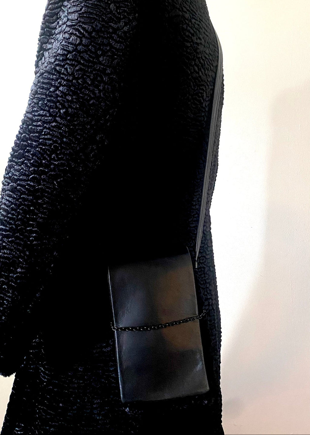 Stacy Stewart Smith Men's Onyx Persian lamb and leather Pocket Messenger bag on a male mannequin wearing a Persian lamb coat by the designer in front of an antique white wall.