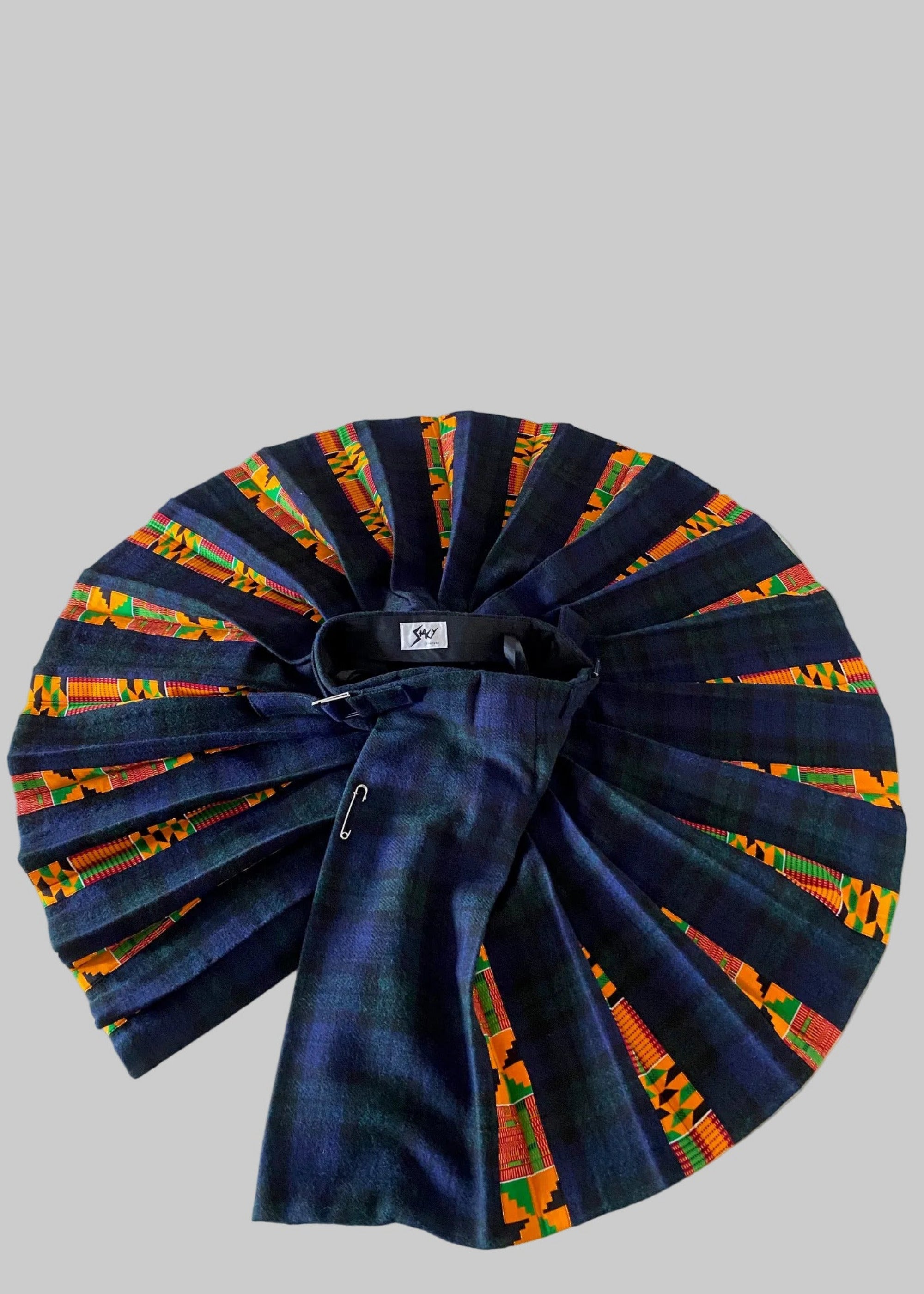 Stacy  Stewart Smith men's Harris Tweed© Blackwatch in blue and green tones Plaid reality Kilt has Kente cloth inlays, chrome side adjustable buckles and kilt open spread from top flat against a plain light surface.