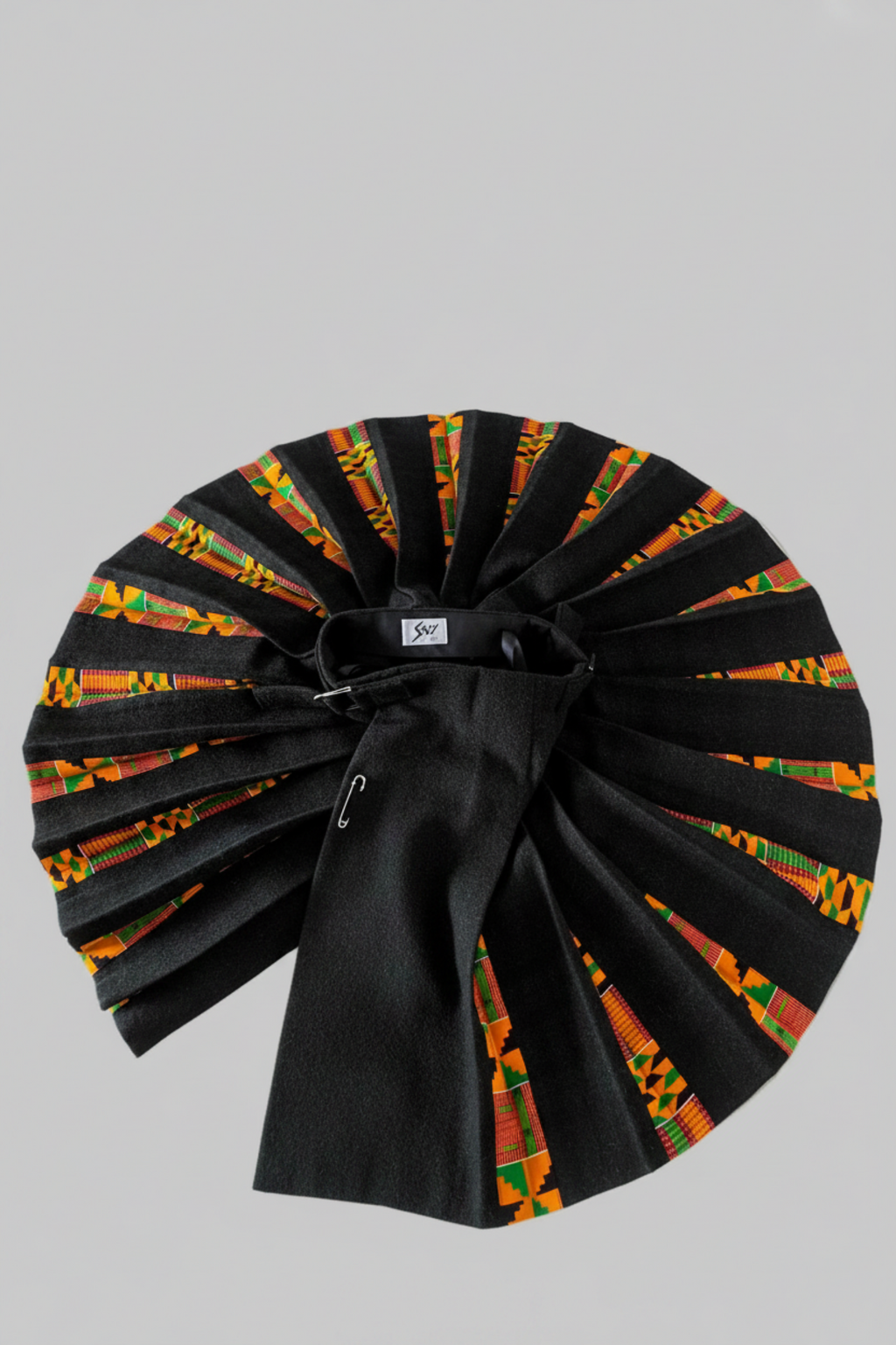 Stacy  Stewart Smith men's Black Harris Tweed© Reality Kilt has Kente cloth inlays, chrome side adjustable buckles and kilt open spread from top flat against a plain light surface.