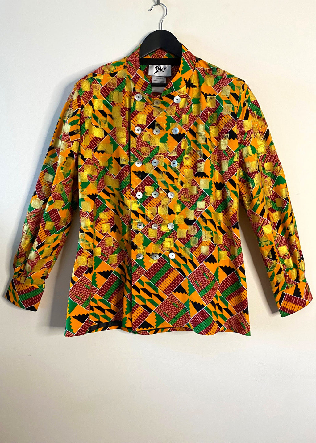 Stacy Stewart Smith's Noble Kente long-sleeve button-up premium cotton Kente cloth dress shirt with manadarin collar, long sleeve gold metallic hand pixel over-printing with natural shell buttons displayed on a hanger front view against a plain wall.
