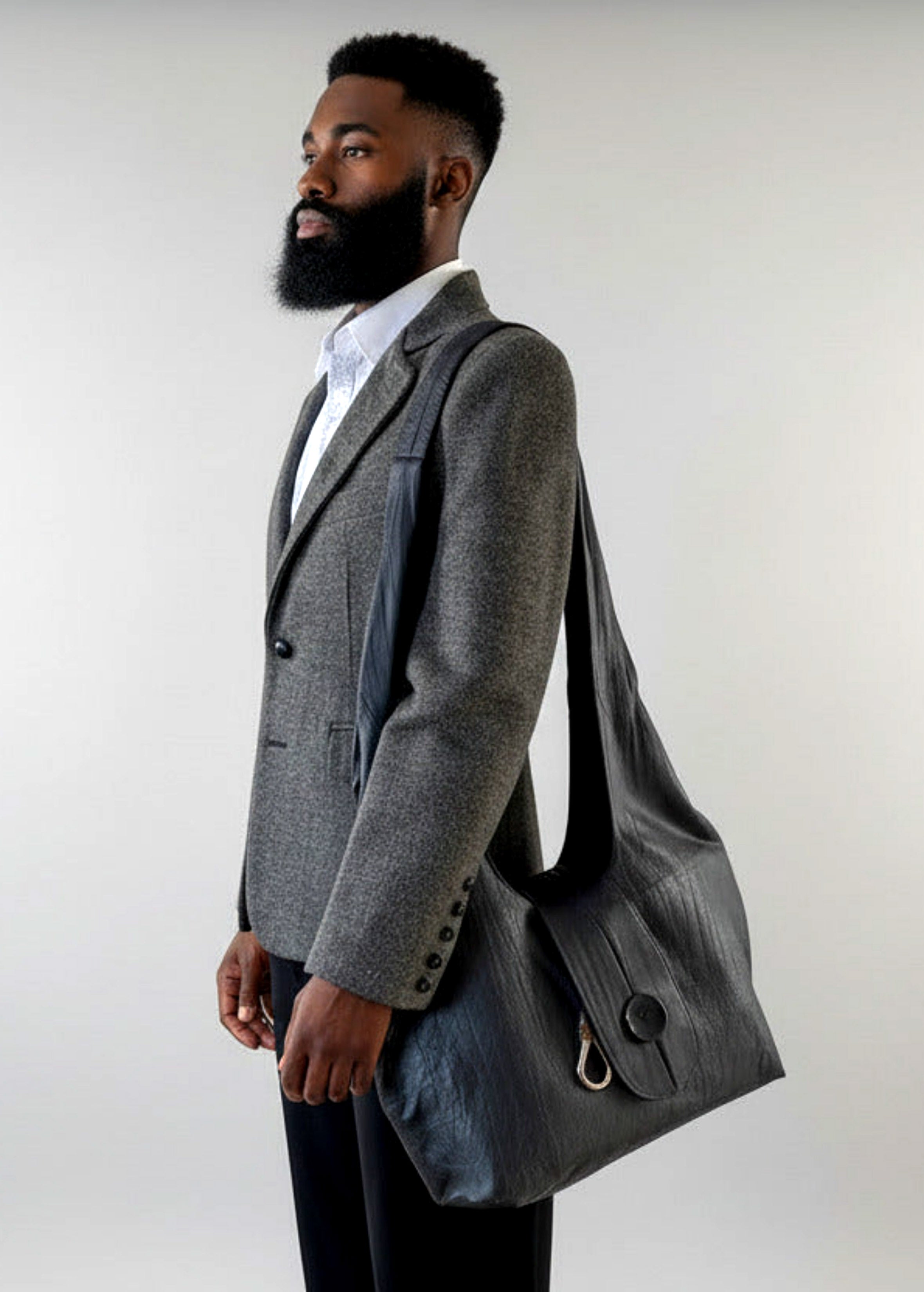 Stacy Stewart Smith Euclidian Space Crinkled Leather Messenger Bag on a mannequin 6'3" wearing the designer's  Diamond Dodger Blazer with black pants in front of a gray backdrop.