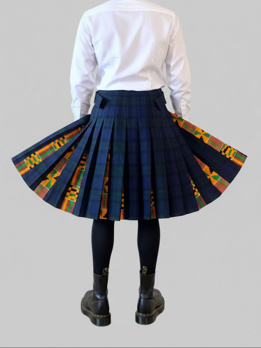 Stacy  Stewart Smith men's Harris Tweed© Blackwatch in blue and green tones Plaid reality Kilt has Kente cloth inlays, chrome side adjustable buckles on a mannequin 6'3" half  front view against a plain light surface. the kilt is shown on a mannequin from the back, styled with a white long-sleeve shirt and black boots against a plain light gray background. The skirt has a dark navy plaid front panel and colorful geometric patterned side panels in orange, yellow, green, and red.