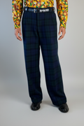 Stacy Stewart Smith's men's  Harris Tweed© Pleated Windsor Pants on a mannequin 6'#" cropped view front. Worn wiith the Noble Kente Kente cloth long-sleeve button-up shirt with a dense multicolor abstract print in yellow, orange, green, and red, with black shoes, standing against a gray backdrop.