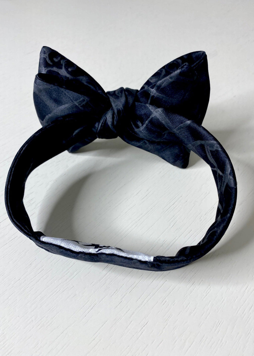 A silk hand-painted black plaid bow tie by Stacy Stewart Smith, back view against a neutral background.