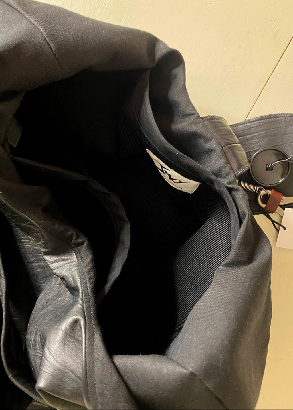 Stacy Stewart Smith Euclidian Space Crinkled Leather Messenger Bag inside view with brand label and pockets showing on an Ivory surface.