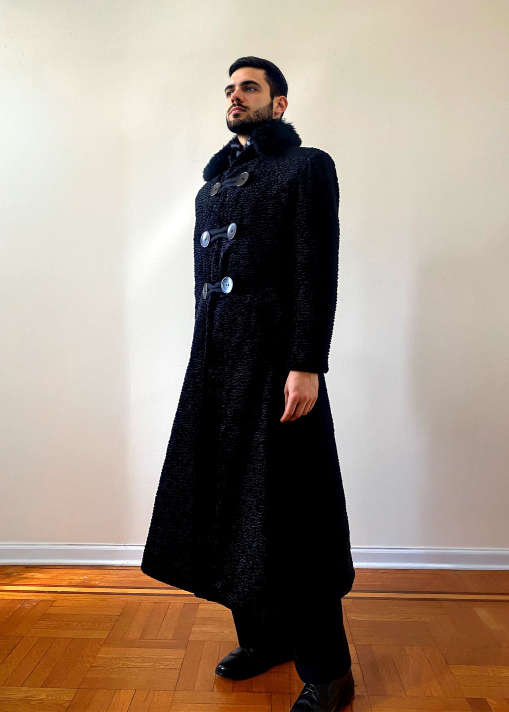Stacy Stewart Smith Men's Night Watchman Faux Persian Lamb Coat with Shearling Collar 3/4 frontal view on a mannequin 6'3" in a room with a wooden floor and an antique white wall.