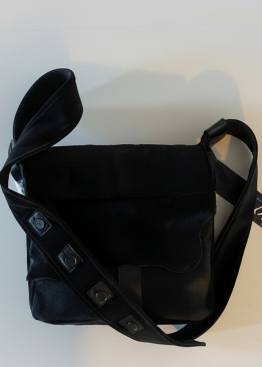 Stacy Stewart Smith Hair-On Calf Powder Satchel Bag back view with buttoned strap  and brand hang-tag on flat surface gray background. 