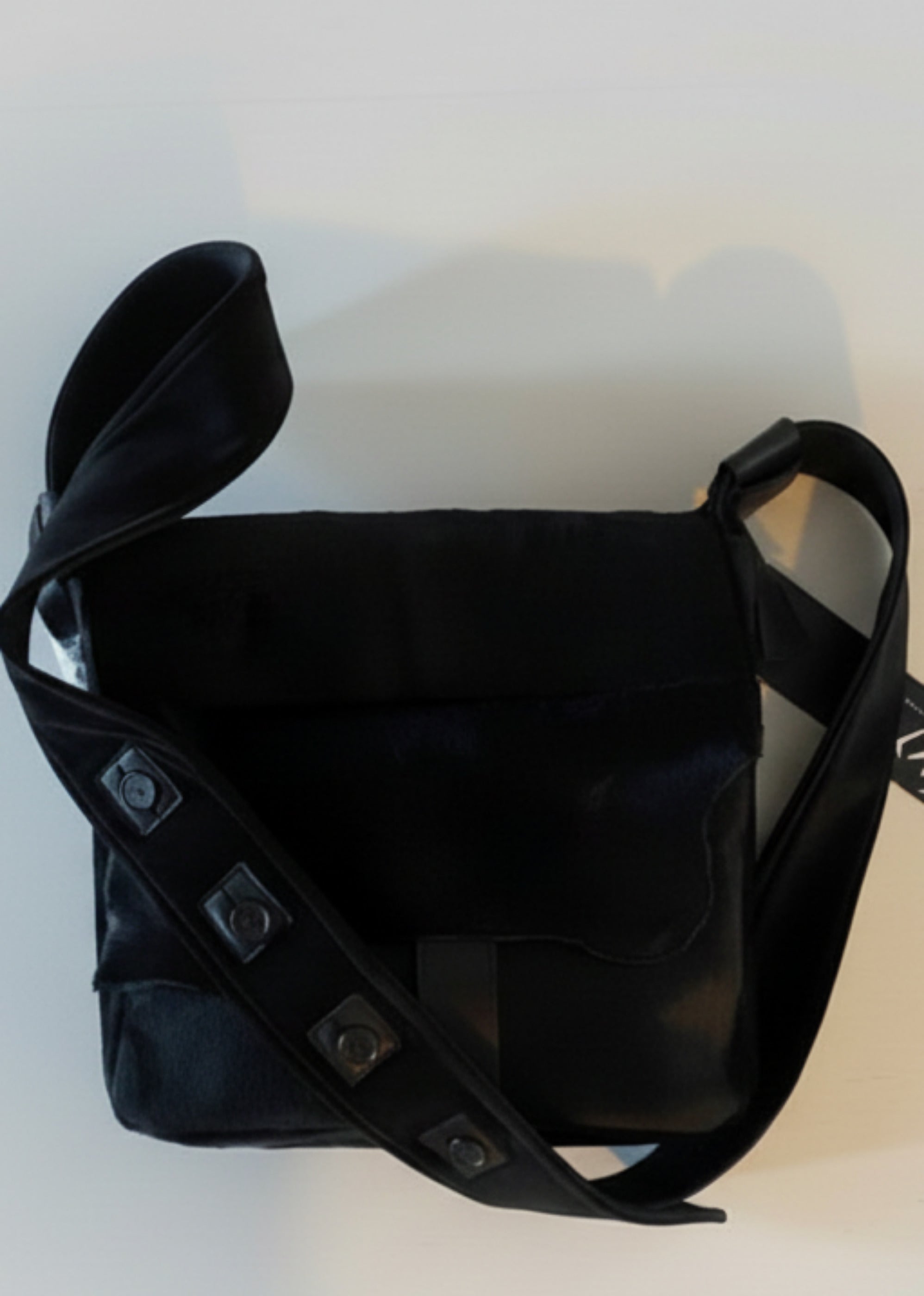 Stacy Stewart Smith Hair-On Calf Powder Satchel Bag back view with buttoned strap  and brand hang-tag on flat surface gray background. 