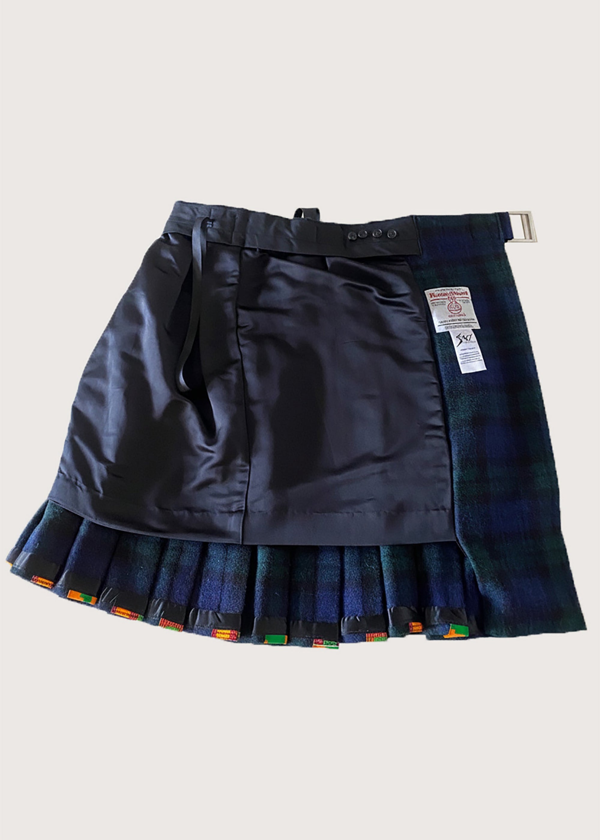 Stacy  Stewart Smith men's Harris Tweed© Blackwatch in blue and green tones Plaid reality Kilt has Kente cloth inlays, chrome side adjustable buckles inside lining flat view against a plain light surface.