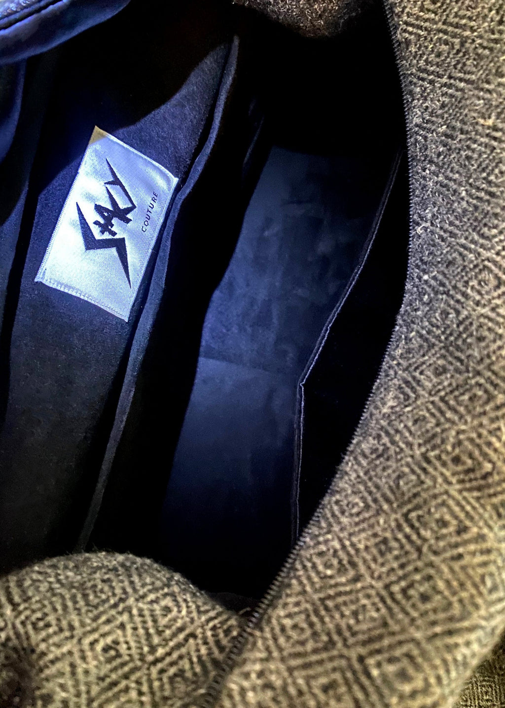 Stacy Stewart Smith's Men's Diamond Dodger Trapezoid messenger bag in Cement/Onyx inside onyx suede lining  view showing Stacy Couture branded label and divider pocket against a gray background.