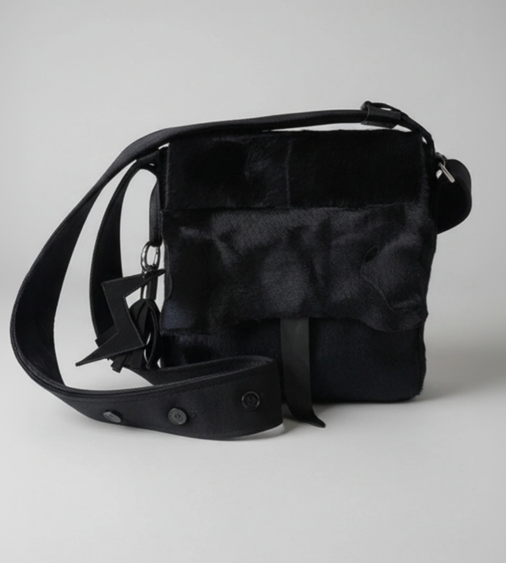 Stacy Stewart Smith's men's black Powder  Bag in Hair-on-Calf hide and Neoprene with a  featuring a wide adjustable strap and a small hanging charm, photographed on a neutral light gray background.