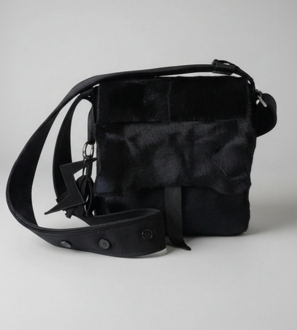 Stacy Stewart Smith's men's black Powder  Bag in Hair-on-Calf hide and Neoprene with a  featuring a wide adjustable strap and a small hanging charm, photographed on a neutral light gray background.
