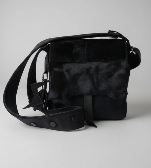 Stacy Stewart Smith's men's black Powder  Bag in Hair-on-Calf hide and Neoprene with a  featuring a wide adjustable strap and a small hanging charm, photographed on a neutral light gray background.