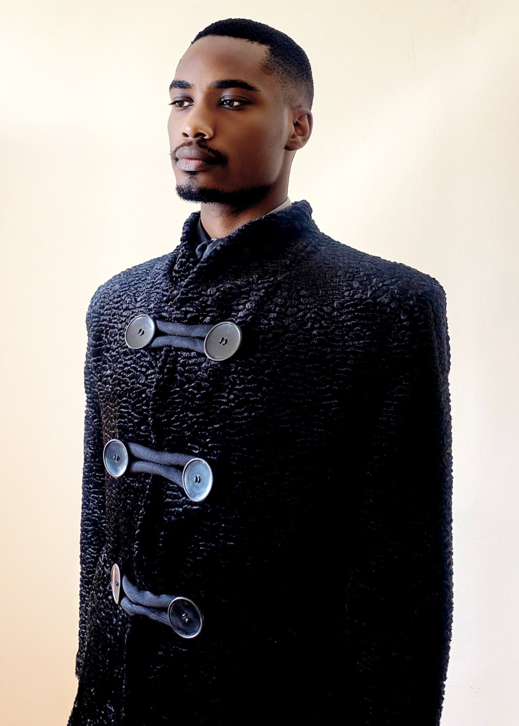 Stacy Stewart Smith Men's Night Watchman Faux Persian Lamb Coat with Shearling Collar zoomed 3/4 frontal view on a mannequin 6'3" in front of a white wall.