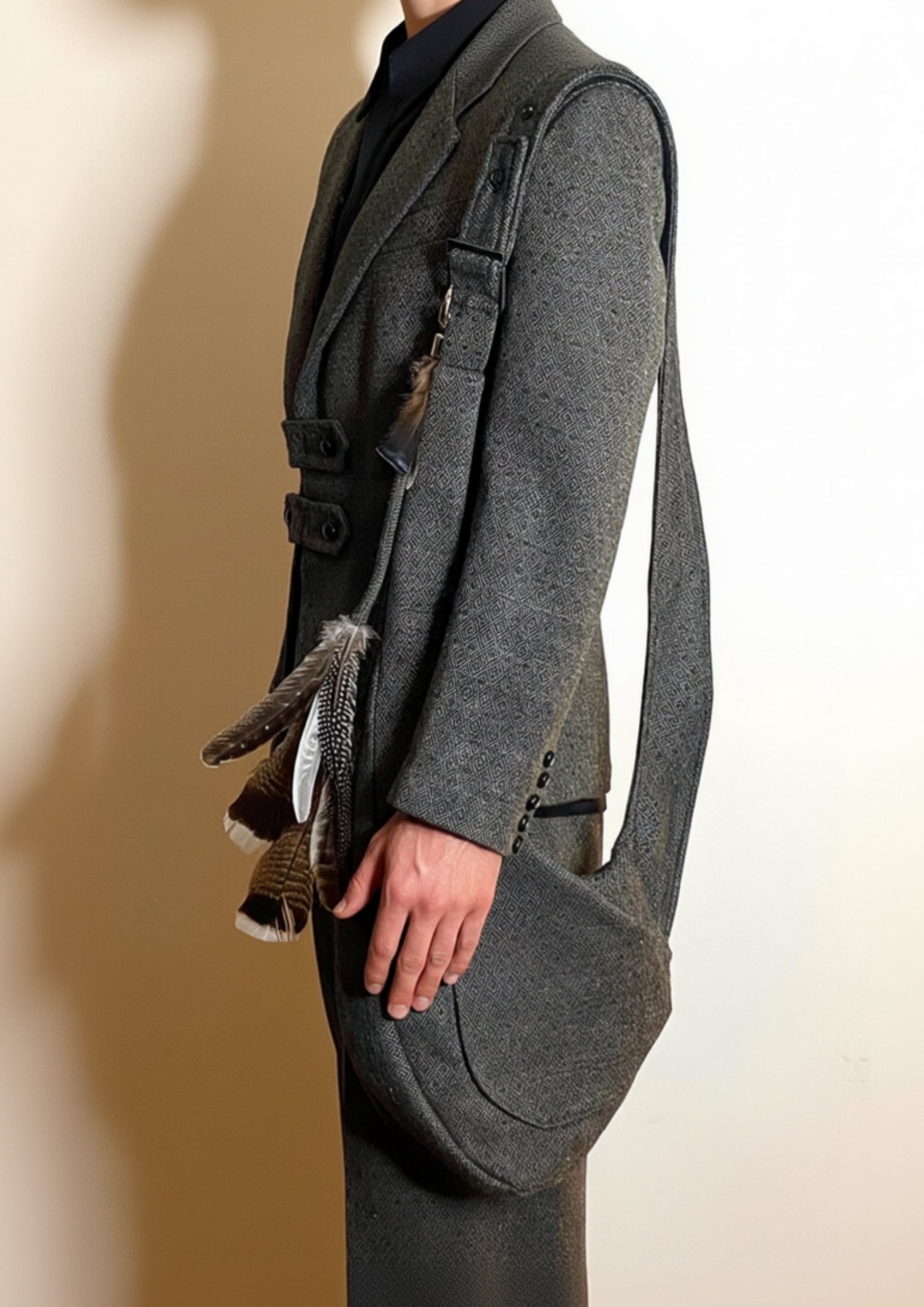 Stacy Stewart Smith Men's Diamond Dodger Tweed Newsie Sling Bag on male model 6'3" side view wearing matching tweed suit in front of an an Ivory wall. 