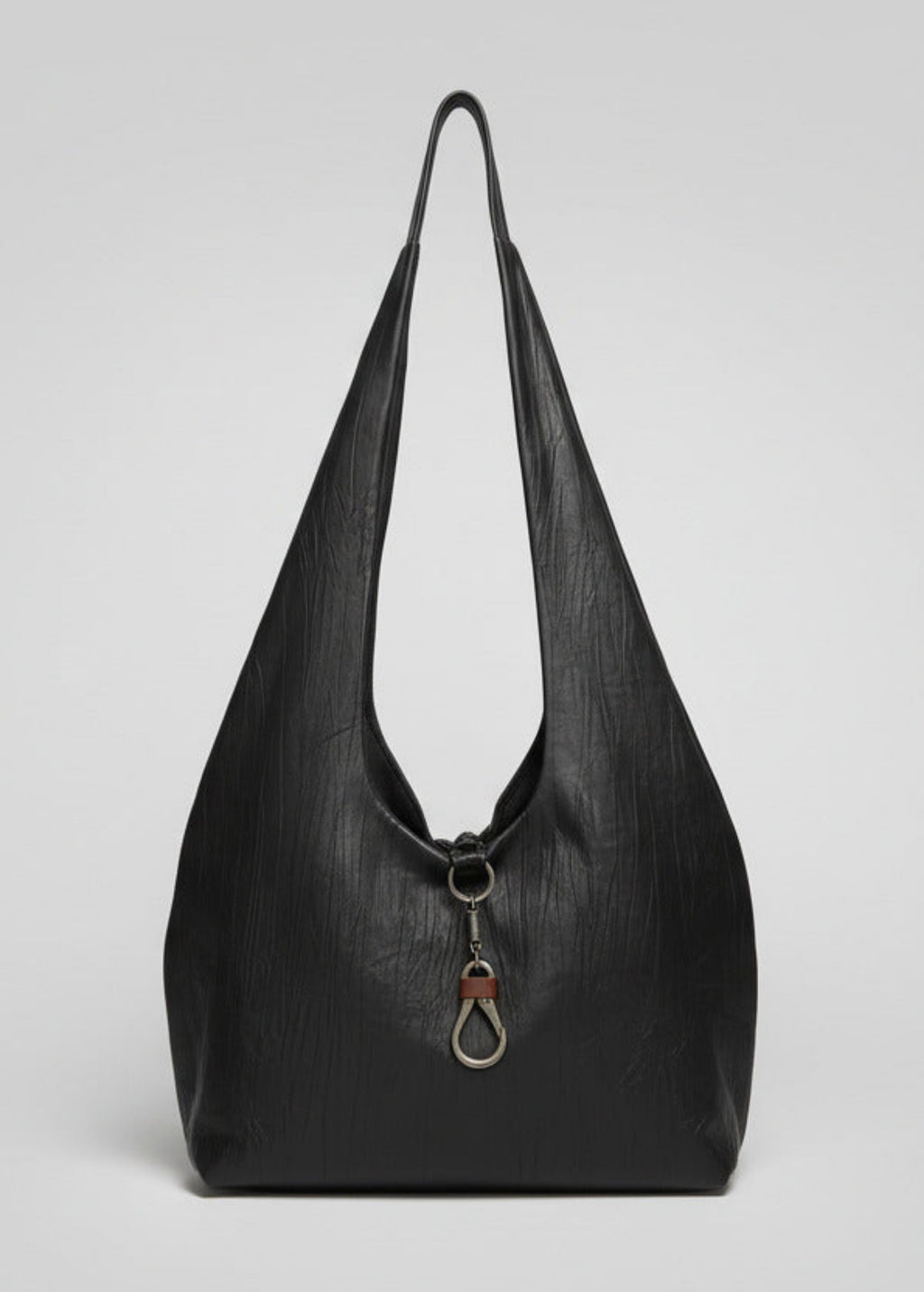 Stacy Stewart Smith Euclidian Space Crinkled Leather Messenger Bag back view view with metal and contrasting leather key holder hanging out over the body in front of a gray backdrop.