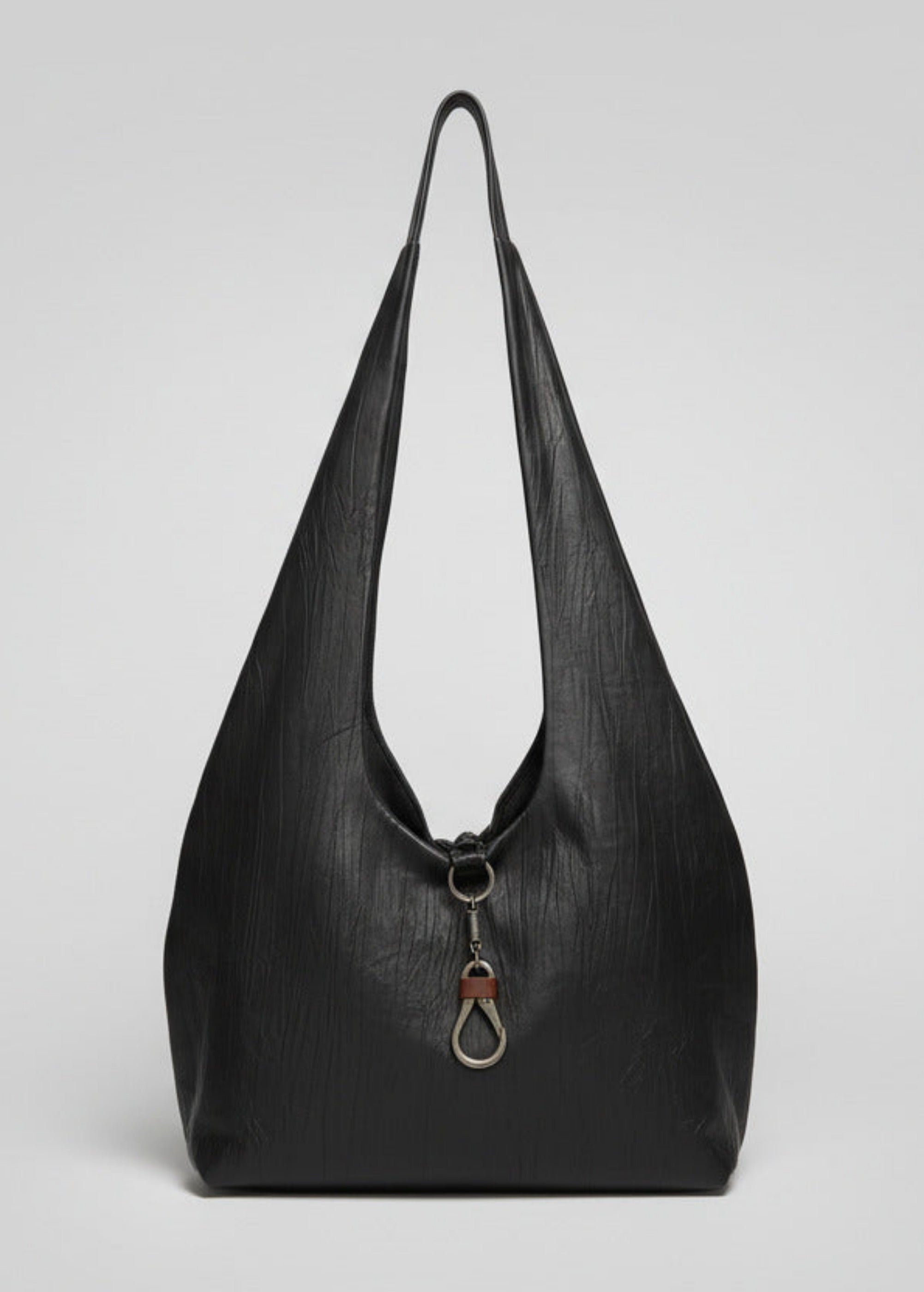 Stacy Stewart Smith Euclidian Space Crinkled Leather Messenger Bag back view view with metal and contrasting leather key holder hanging out over the body in front of a gray backdrop.