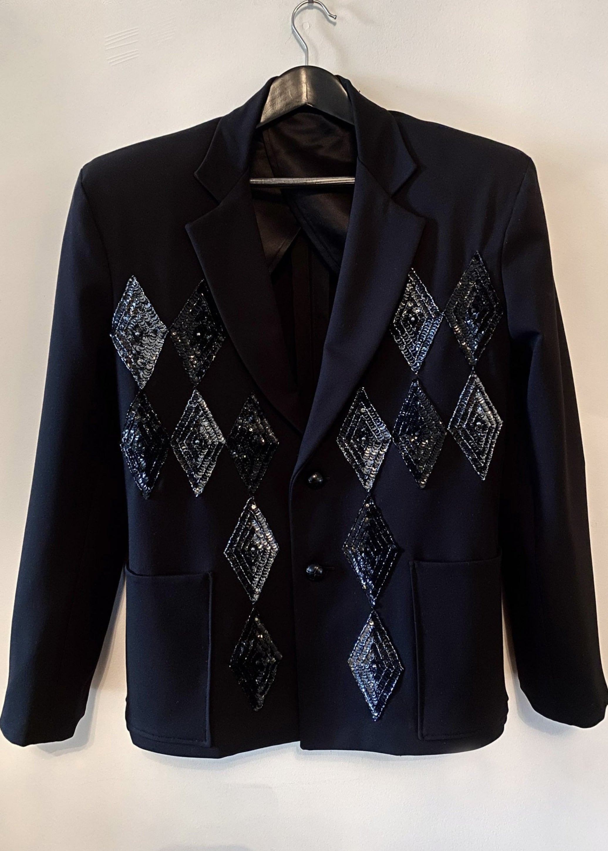 Stacy Stewart Smith Men's Black Knit, Sequin and Beaded Harlequin Blazer on a hanger with antique white wall.