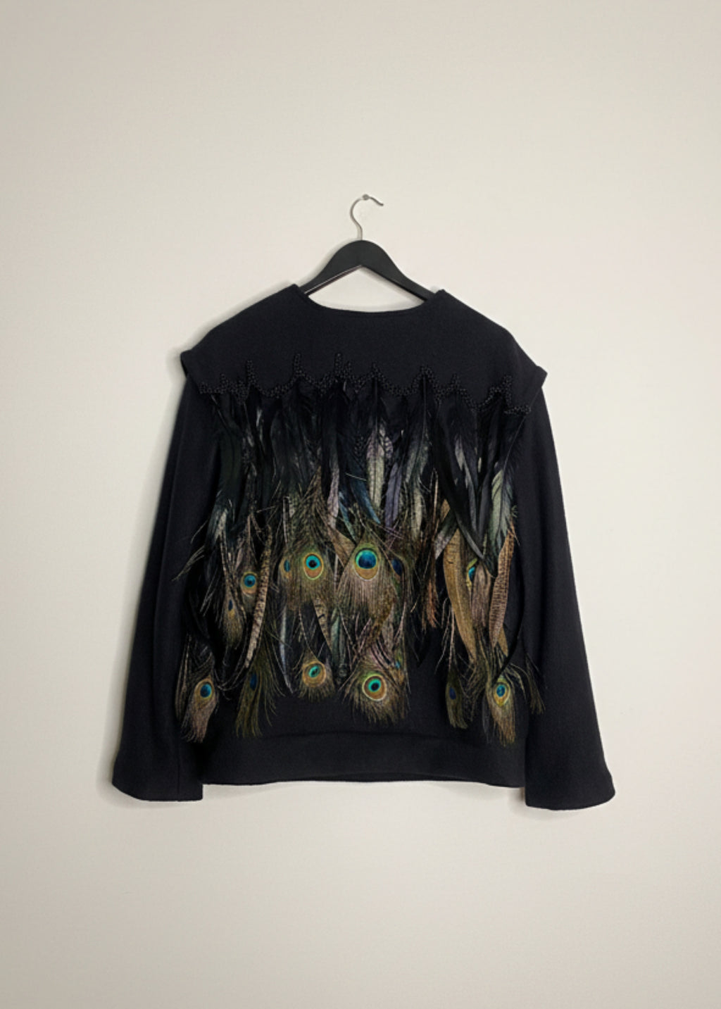 Stacy Stewart Smith Men's Pennaceous Beaded Black Boiled Wool Sweater with peacock, quail and rooster feathers on a hanger back view  against an ivory backdrop. 