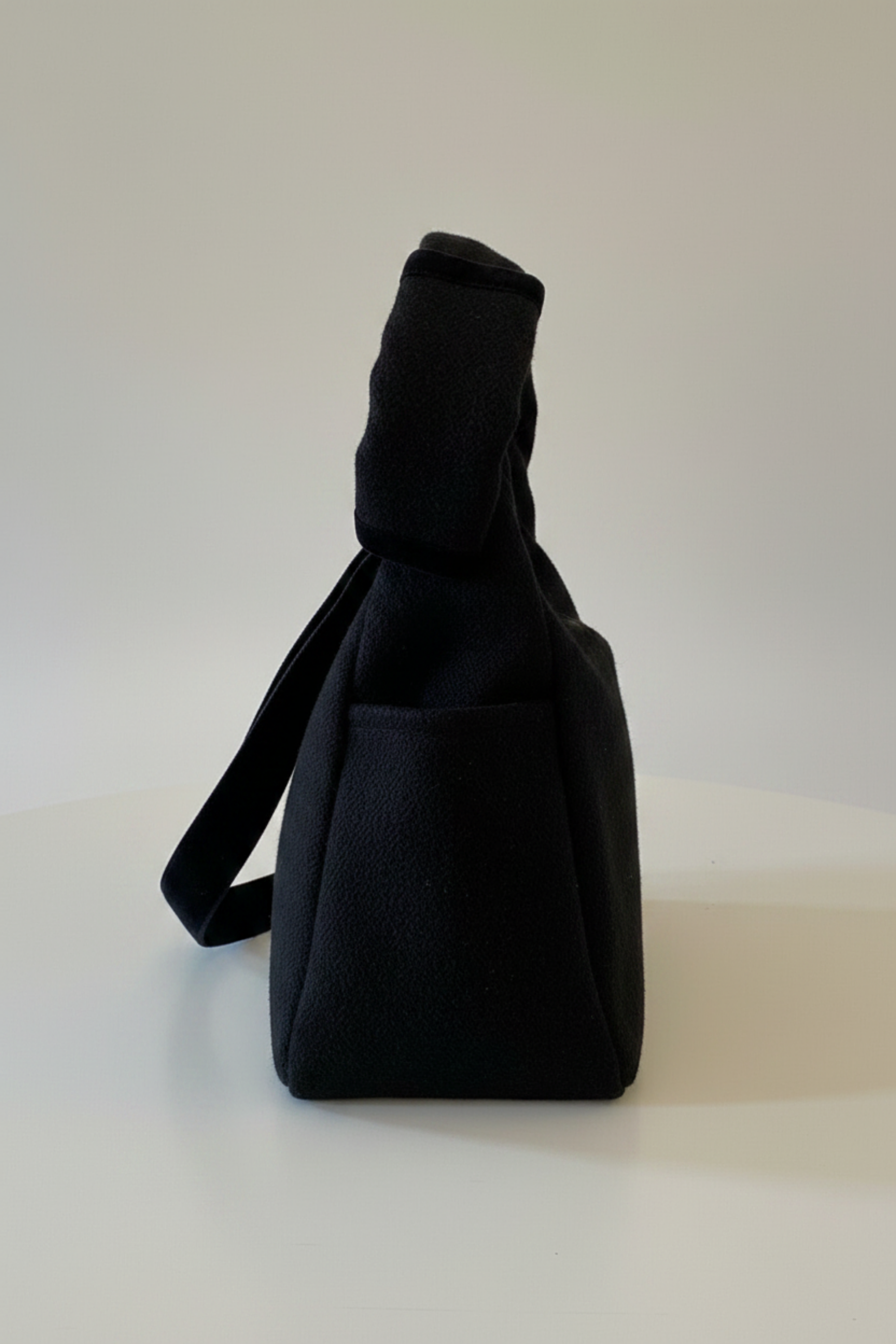 Stacy Stewart Smith's Men's Onyx Harris Tweed® Trapezoid messenger bag with  d the shoulder strap folded side view against a gray background.