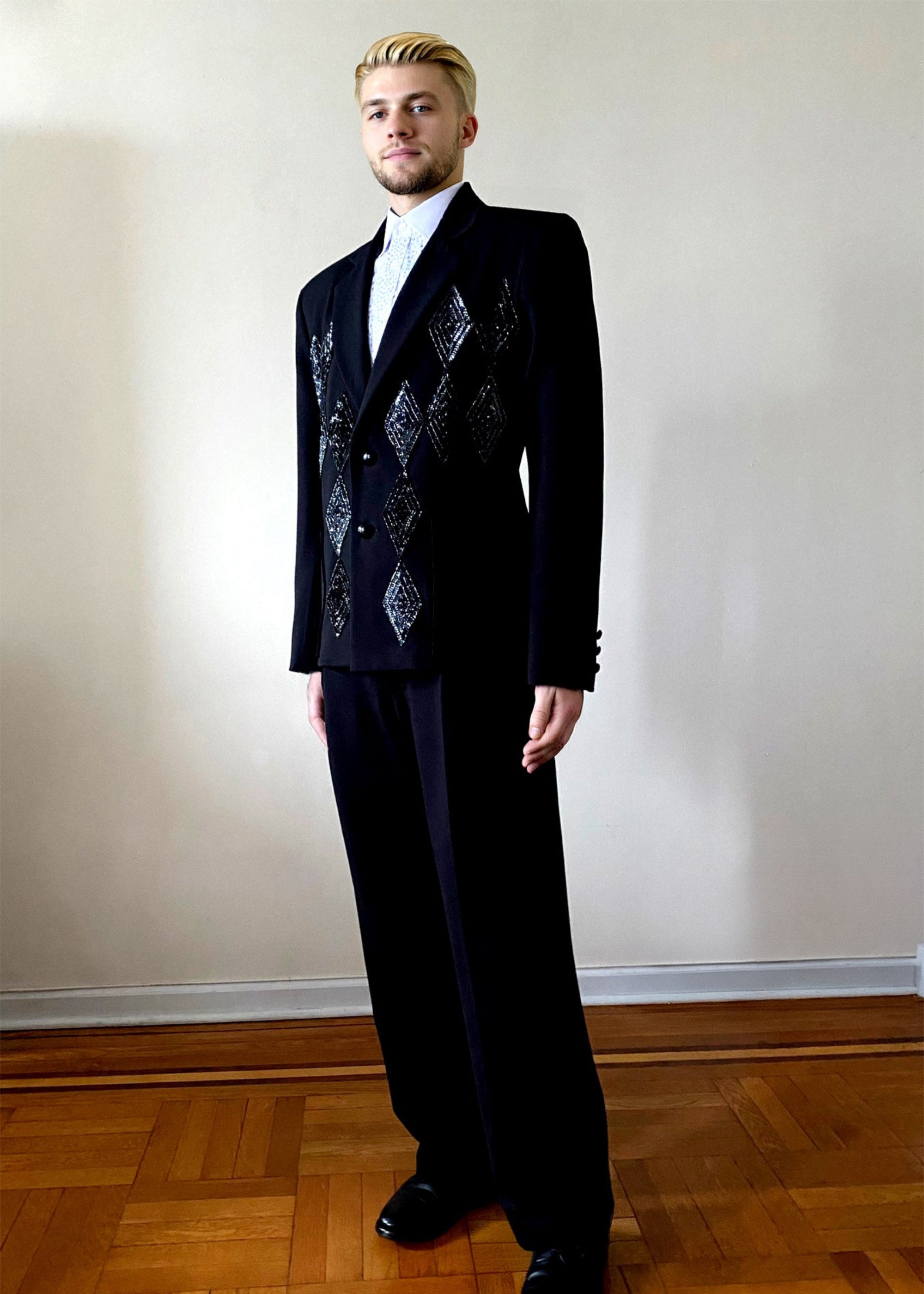Stacy Stewart Smith Men's Black Knit, Sequin and Beaded Harlequin Blazer on a mannequin 6'3" full body 3/4 pose with hand painted shirt in a room with a wood floor and antique white wall.