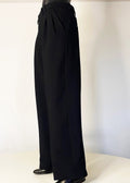 Stacy Stewart Smith Men's Black Knit Pleated Windsor Pants 3/4 view on mannequin 6'3" with ivory backdrop. 