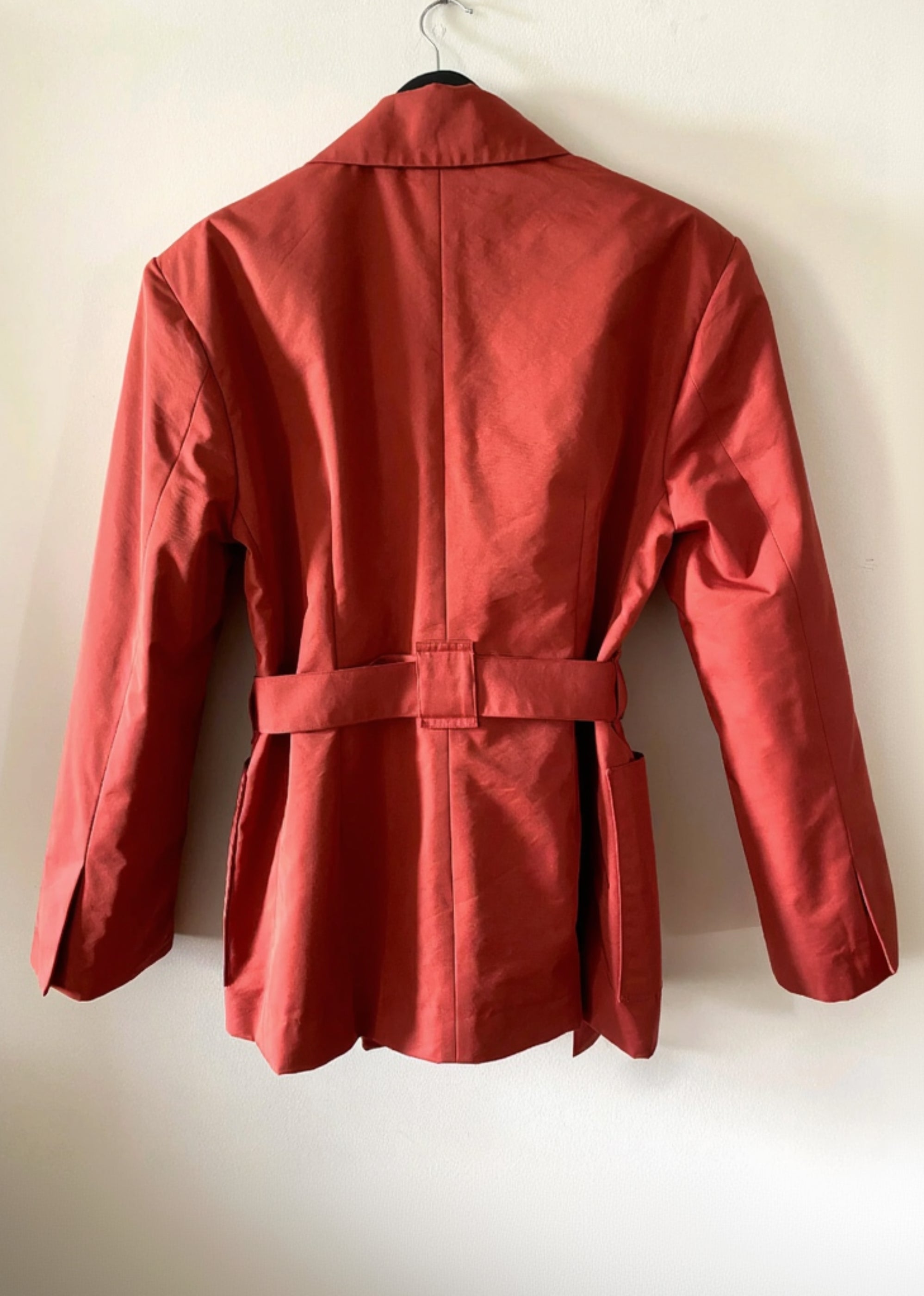 7. Sky & Ruby Trench-Jack back view on a hanger against an antique white wall.