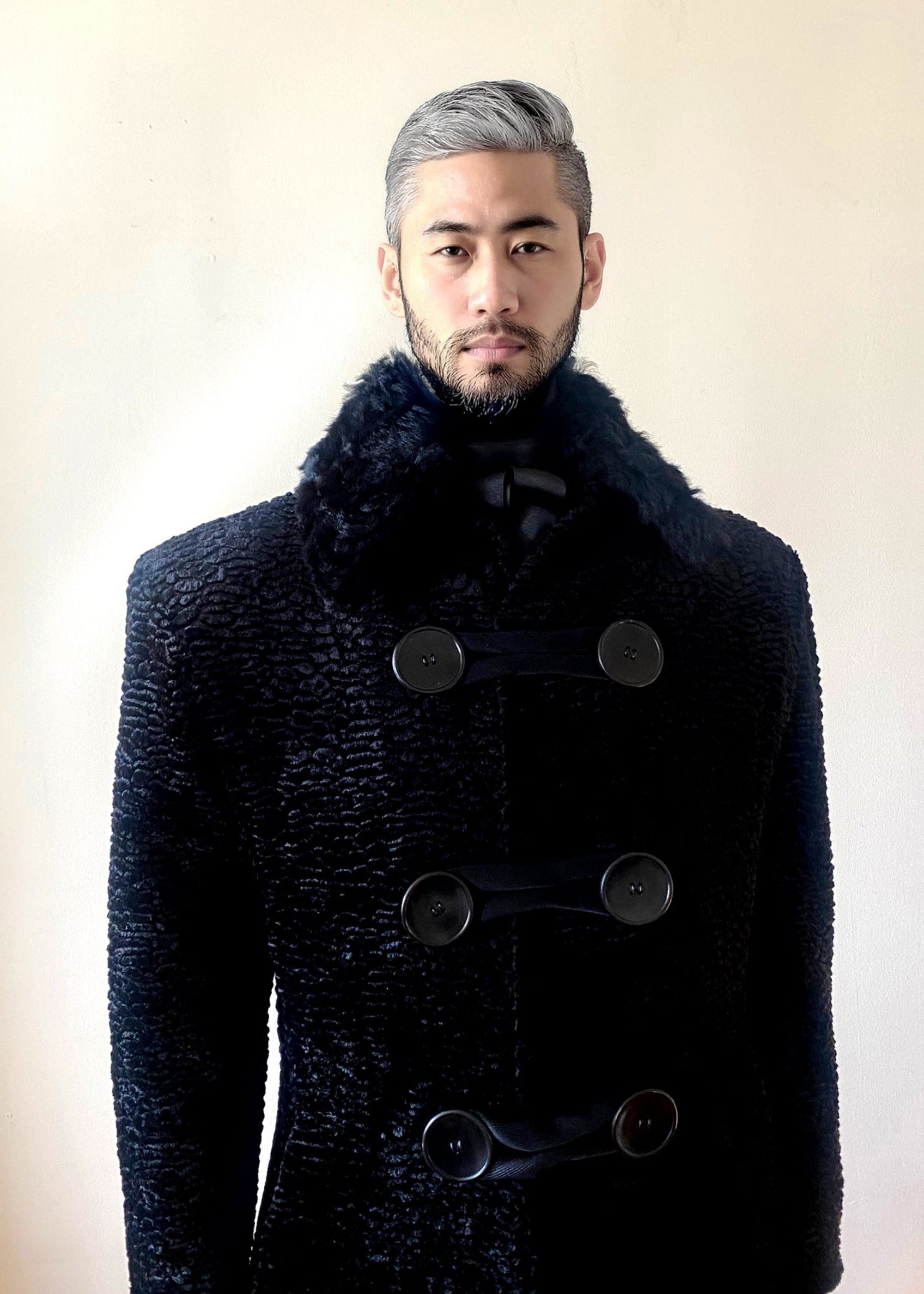 Stacy Stewart Smith Men's Night Watchman Faux Persian Lamb Coat with Shearling Collar zoomed frontal view on a mannequin 6'3" in a room an antique white wall.