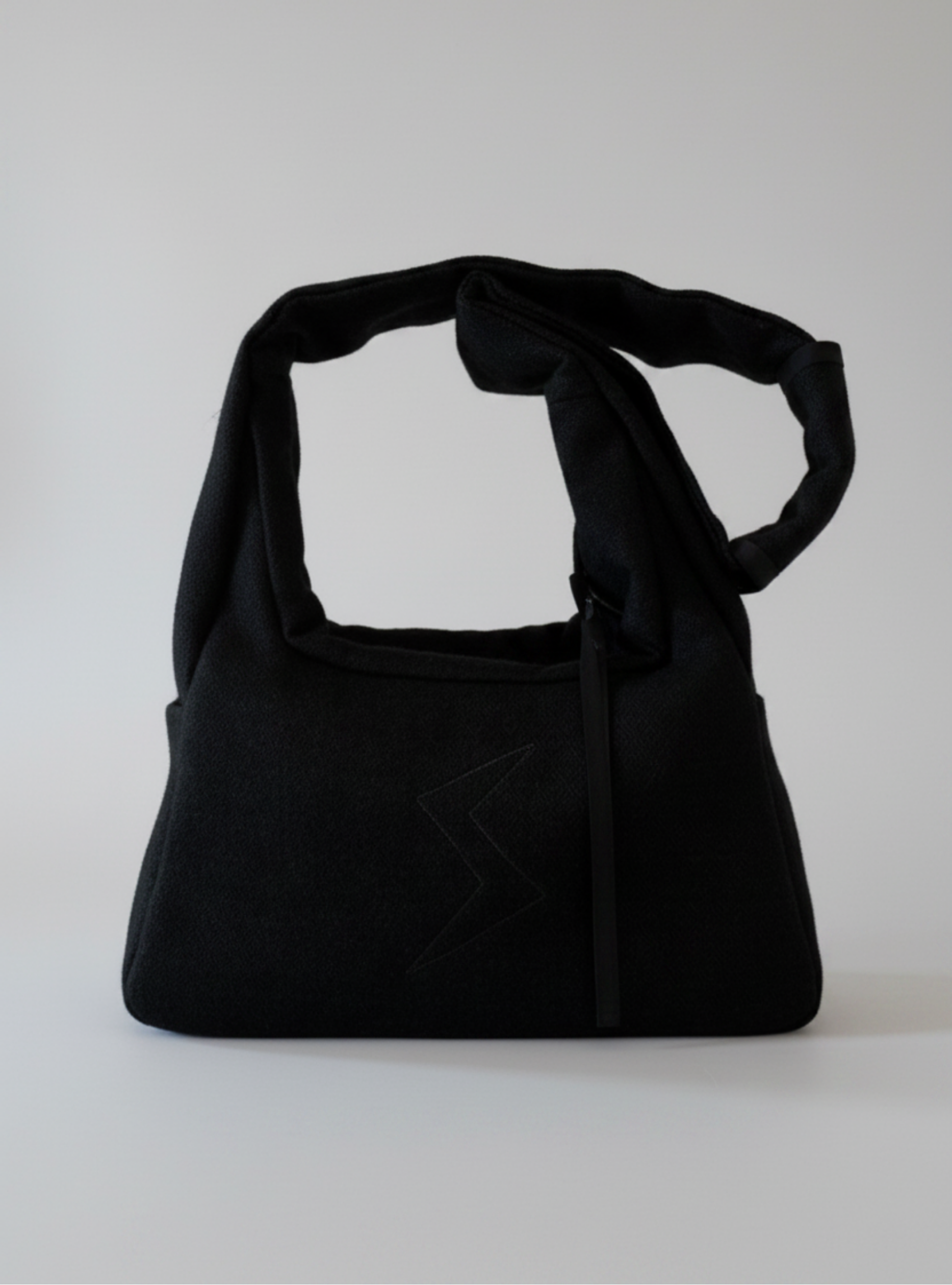 Stacy Stewart Smith's Men's Onyx Harris Tweed® Trapezoid messenger bag with  house logo embroidery and the shoulder strap folded frontal view against a gray background.