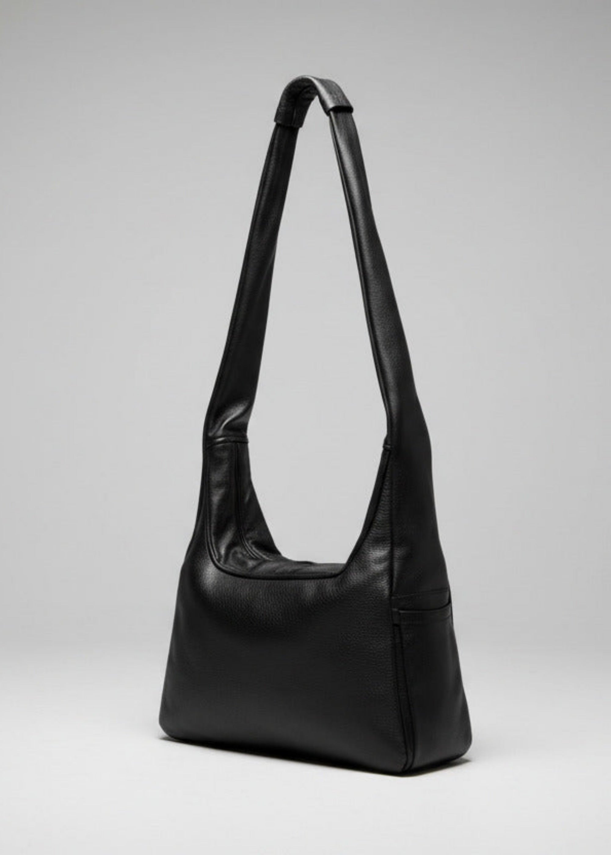 Stacy Stewart Smith Trapezoid Leather Messenger Bag in Onyx frontal 3/4 view with the strap standing up in front of a light gray backdrop.