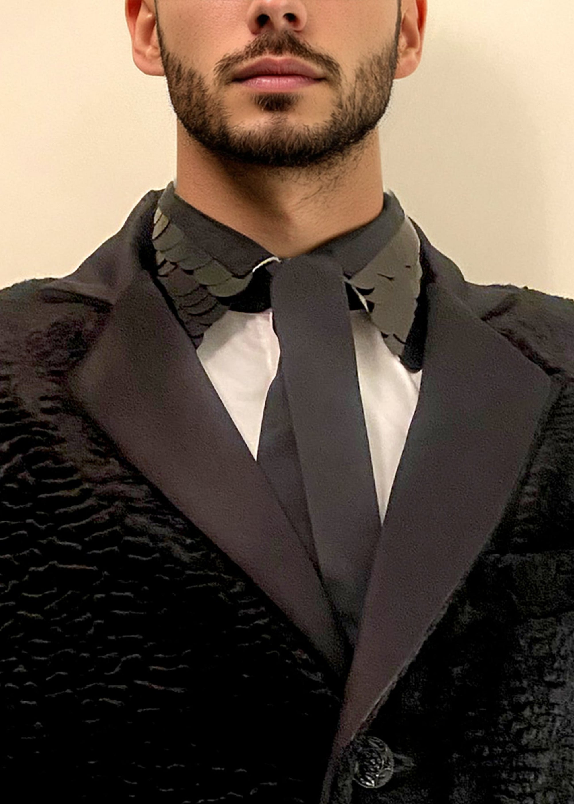 Stacy Stewart Smith Men's Leviathan Scales Western Tuxedo Shirt zoomed front view tie down in black faux Persian lamb tuxedo against antique white wall. 