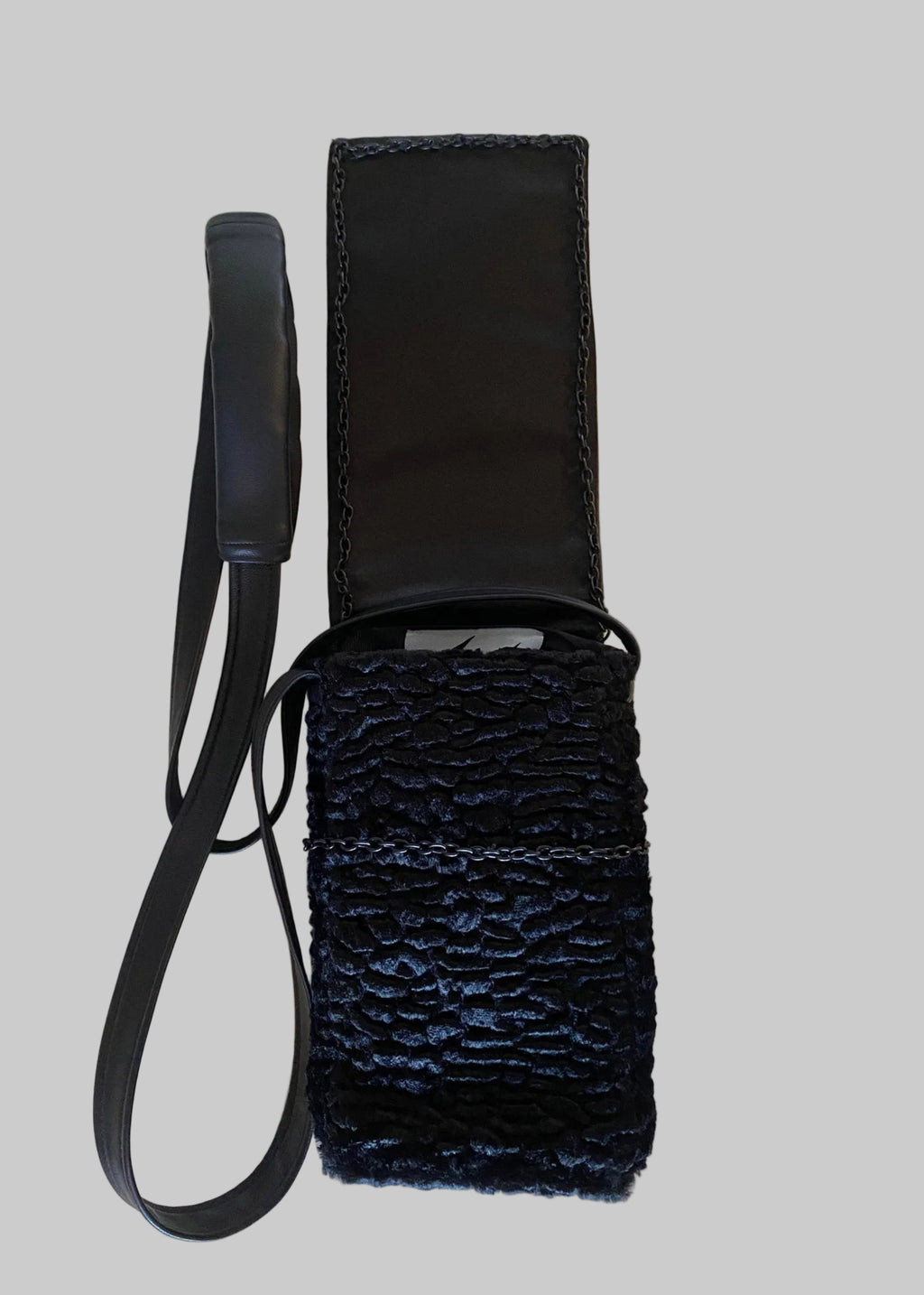 Stacy Stewart Smith Onyx Persian lamb and leather Pocket Messenger  bag with a strap flat on a gray surface with flap up exposing brand lalbel and chain weight flap.
