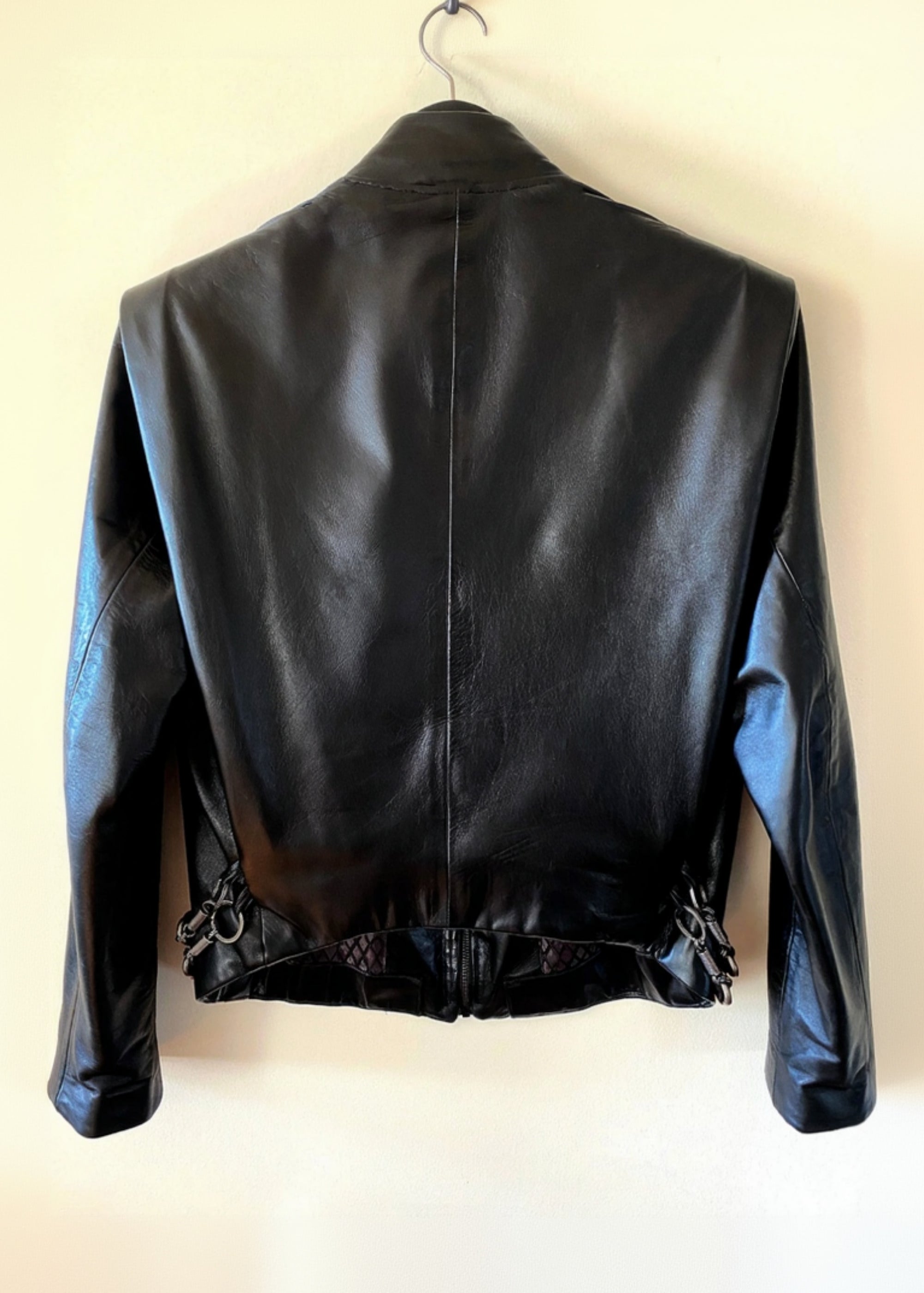 Stacy Stewart Smith Men's Flange-Back Leather Moto Jacket hanging back view against an antique white background.