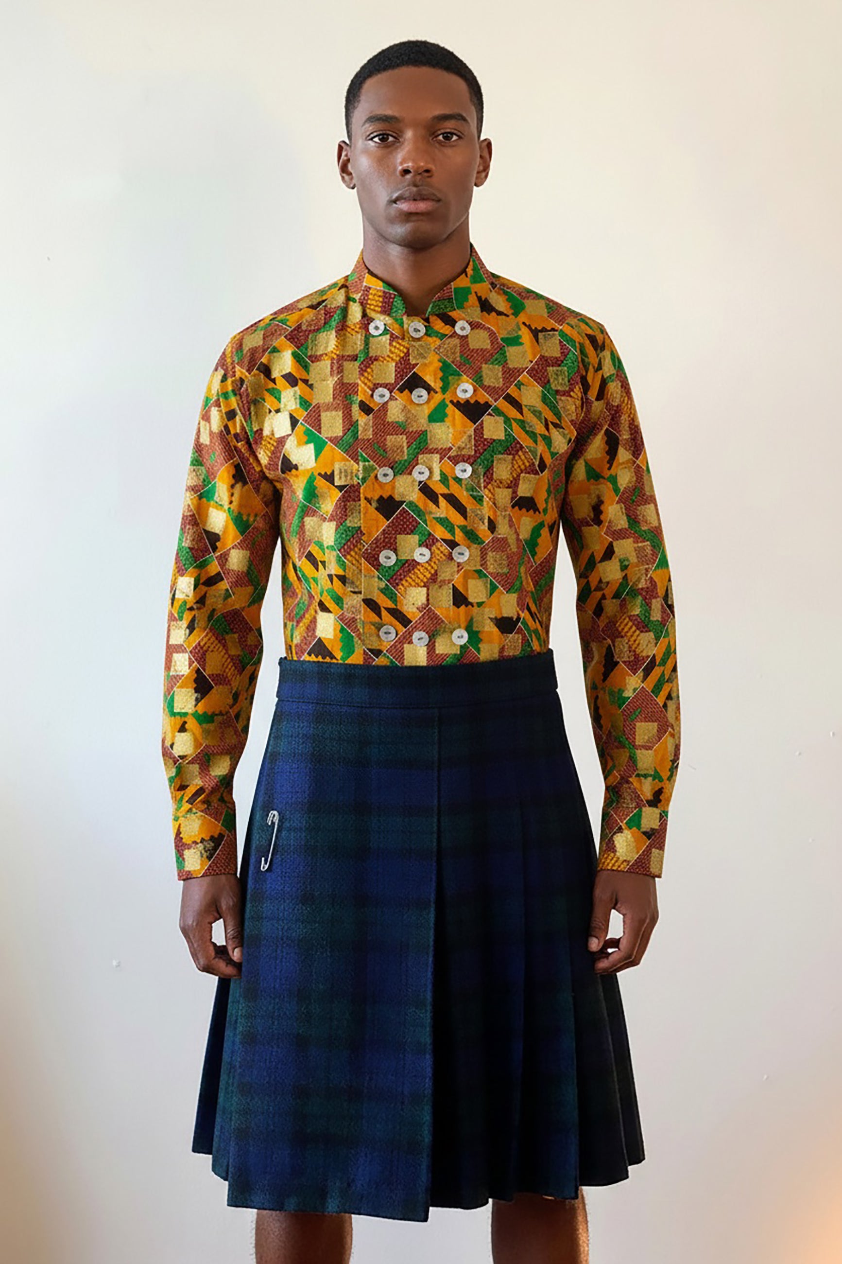 Stacy Stewart Smith's Noble Kente long-sleeve button-up premium cotton Kente cloth dress shirt with manadarin collar, long sleeve gold metallic hand pixel over-printing and real shell buttons styled with Blackwatch plaid Reality Kilt on a male model torso front view against a plain wall.