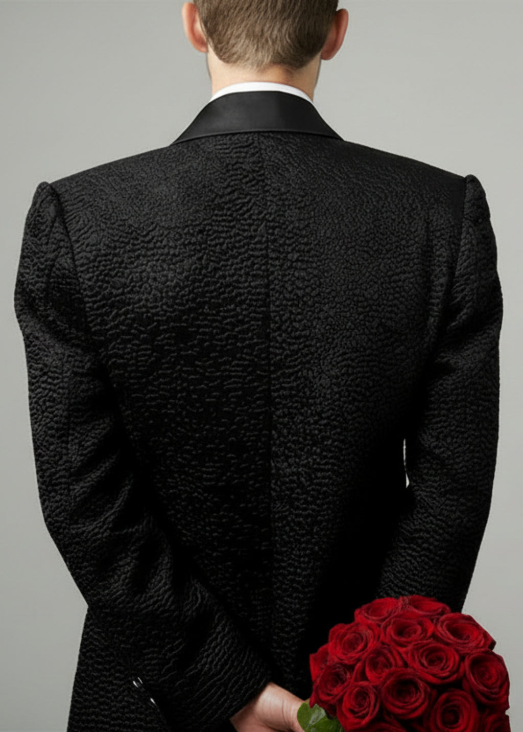 Stacy Stewart Smith Men's Faux Persian lamb Edwardian Abbreviated Tuxedo jacket, shown on mannequin at 6'3 holding red roses from the back view.