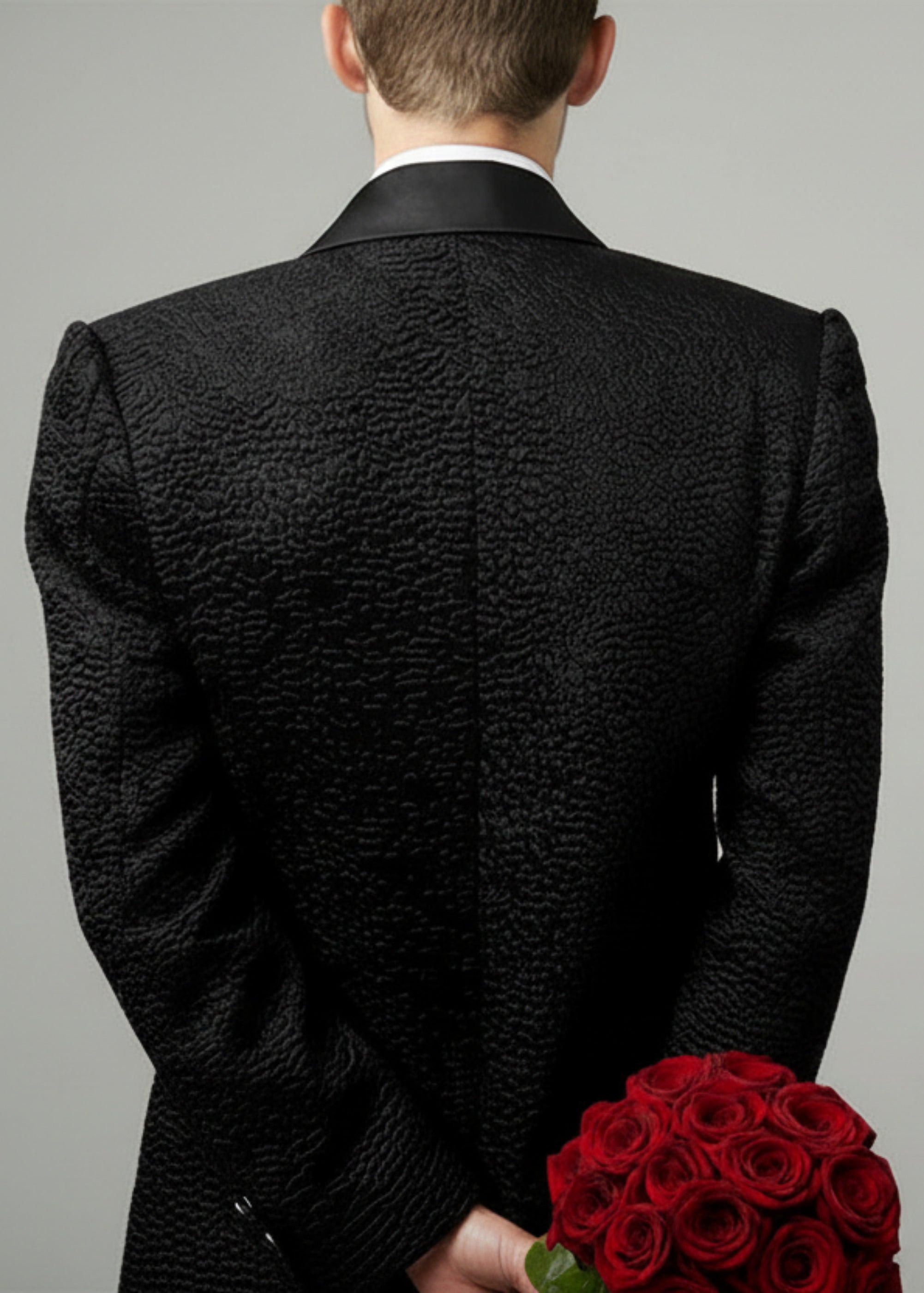 Stacy Stewart Smith Men's Faux Persian lamb Edwardian Abbreviated Tuxedo jacket, shown on mannequin at 6'3 holding red roses from the back view.