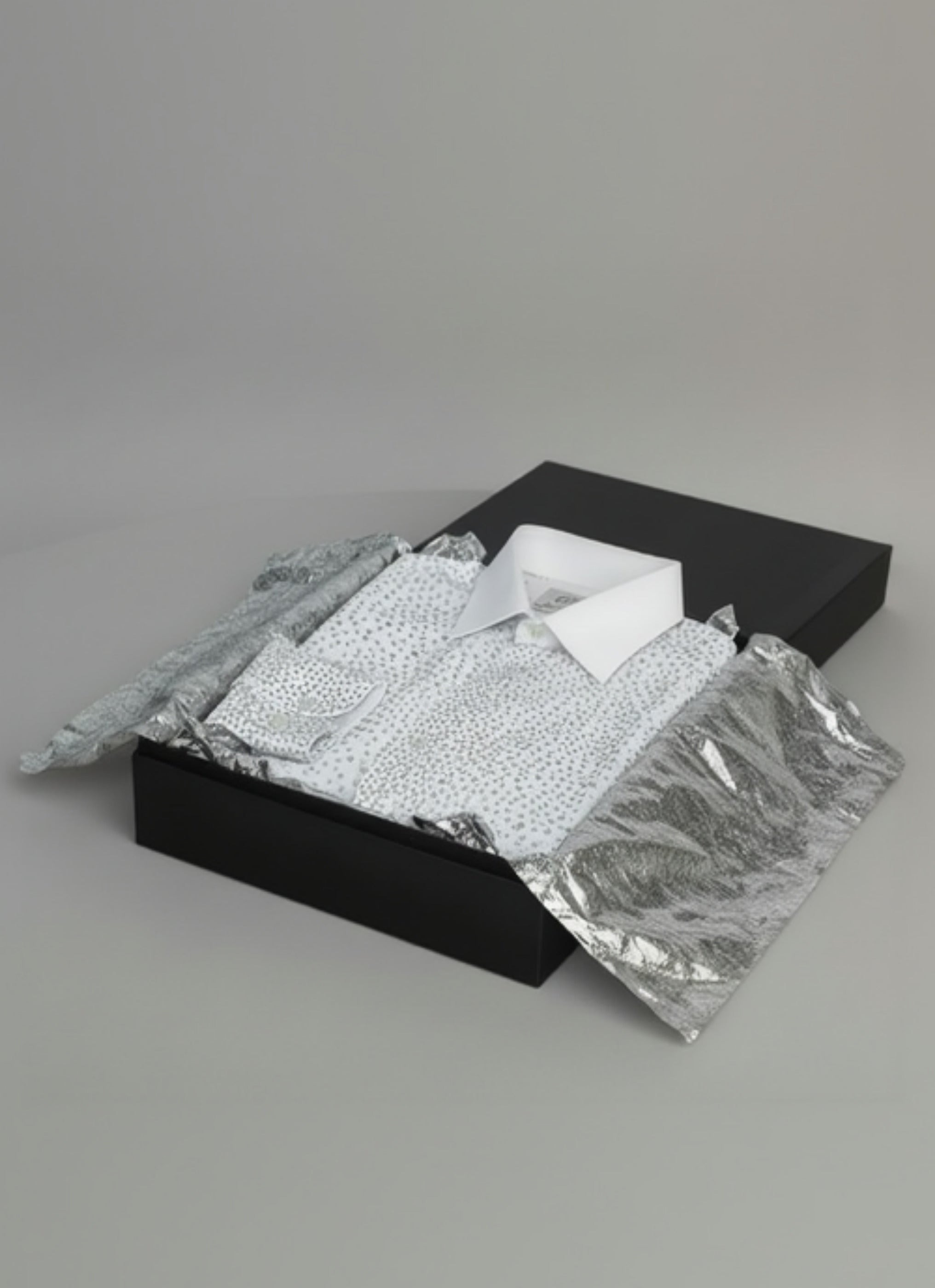 Stacy Stewart Smith Men's Silver Angels White Premium Cotton Percale Hand-Painted Shirt folded in a black gift box with silver tissue paper on a gray  backdrop.