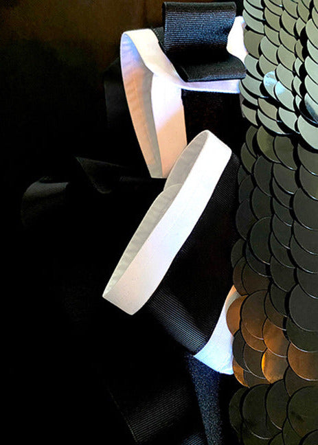 Example of Stacy Stewart Smith Leviathan Scales Onyx-White | Limited Edition Digital Collectible shows the black paillette clustered collar and white cuffs trrimmed with black grosgrain ribbon arranged vertically flat on a black satin covered surface in Art Deco styling