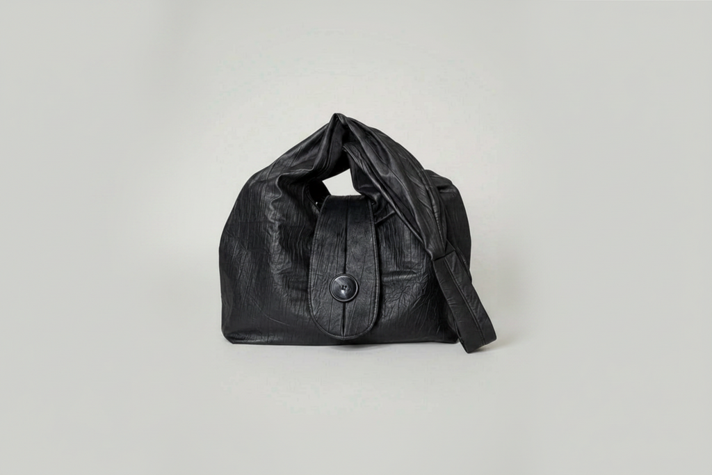 Stacy Stewart Smith Euclidean Space Crinkled Leather Messenger Bag with handle down on a white surface and backdrop.