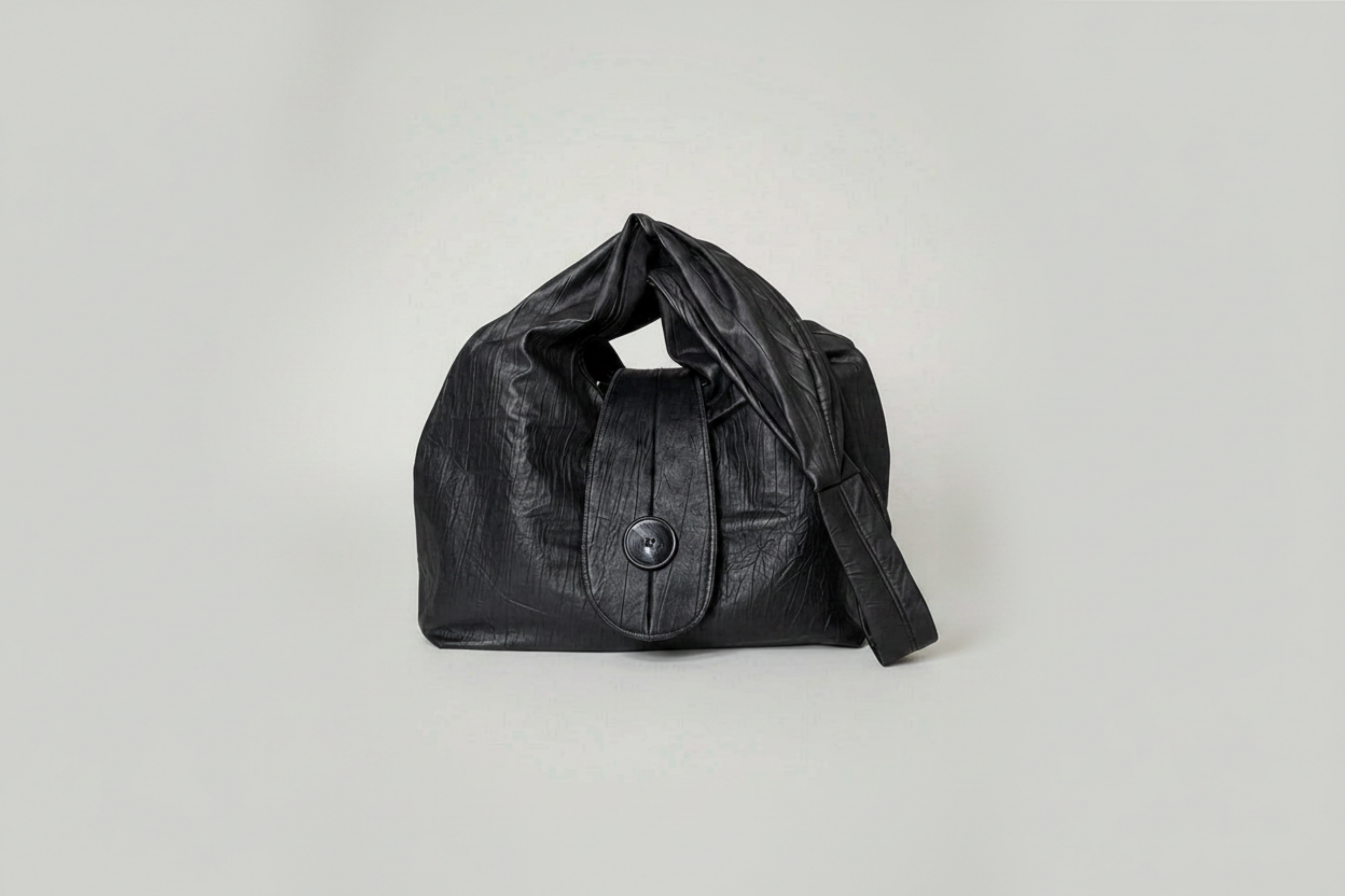 Stacy Stewart Smith Euclidean Space Crinkled Leather Messenger Bag with handle down on a white surface and backdrop.