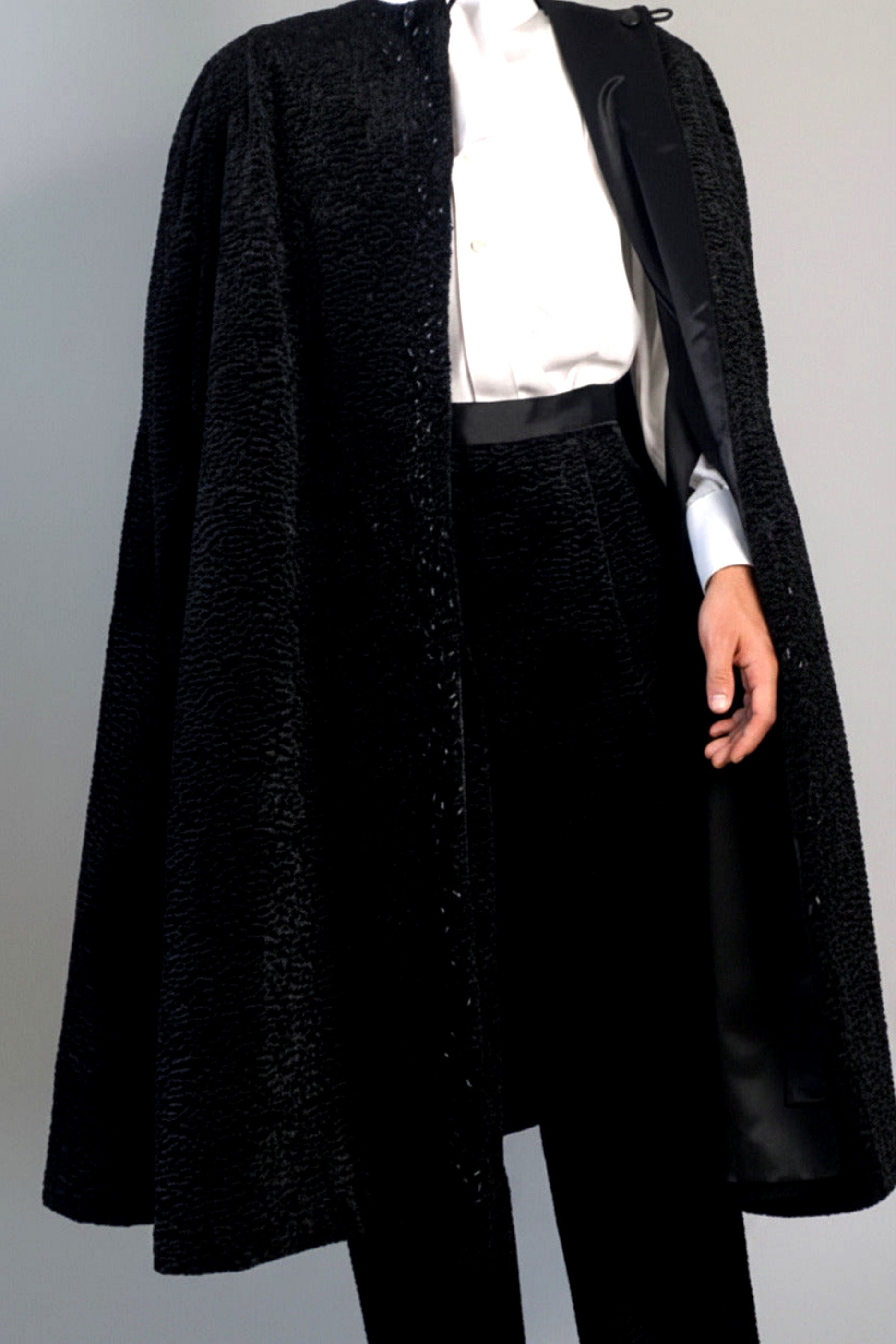 The Grand Soir Palace Cape by Stacy  Stewart Smith is cut for exactly that moment — a structured sweep of flowing black Persian lamb on a mannequin 6'3" against a gray backdrop. Front view with  cape fully open to show bugle beading, neckline loops, and one arm through inside satin lining and holder, which also reveals the matching Grand Soir Tuxedo trousers.
