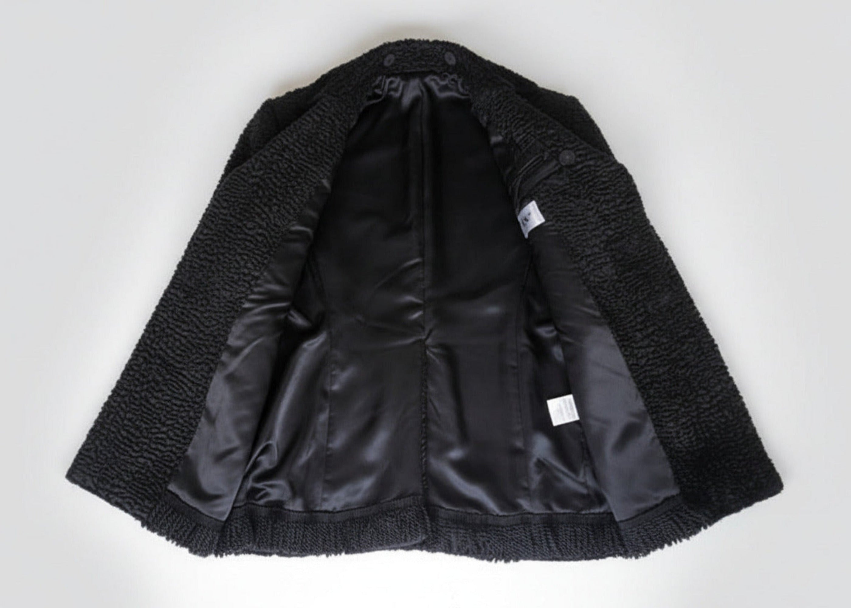 Stacy Stewart Smith Men's Black Knight Faux Persian Lamb Coat in Coal Black, shown open on flat surface revealing lining details.
